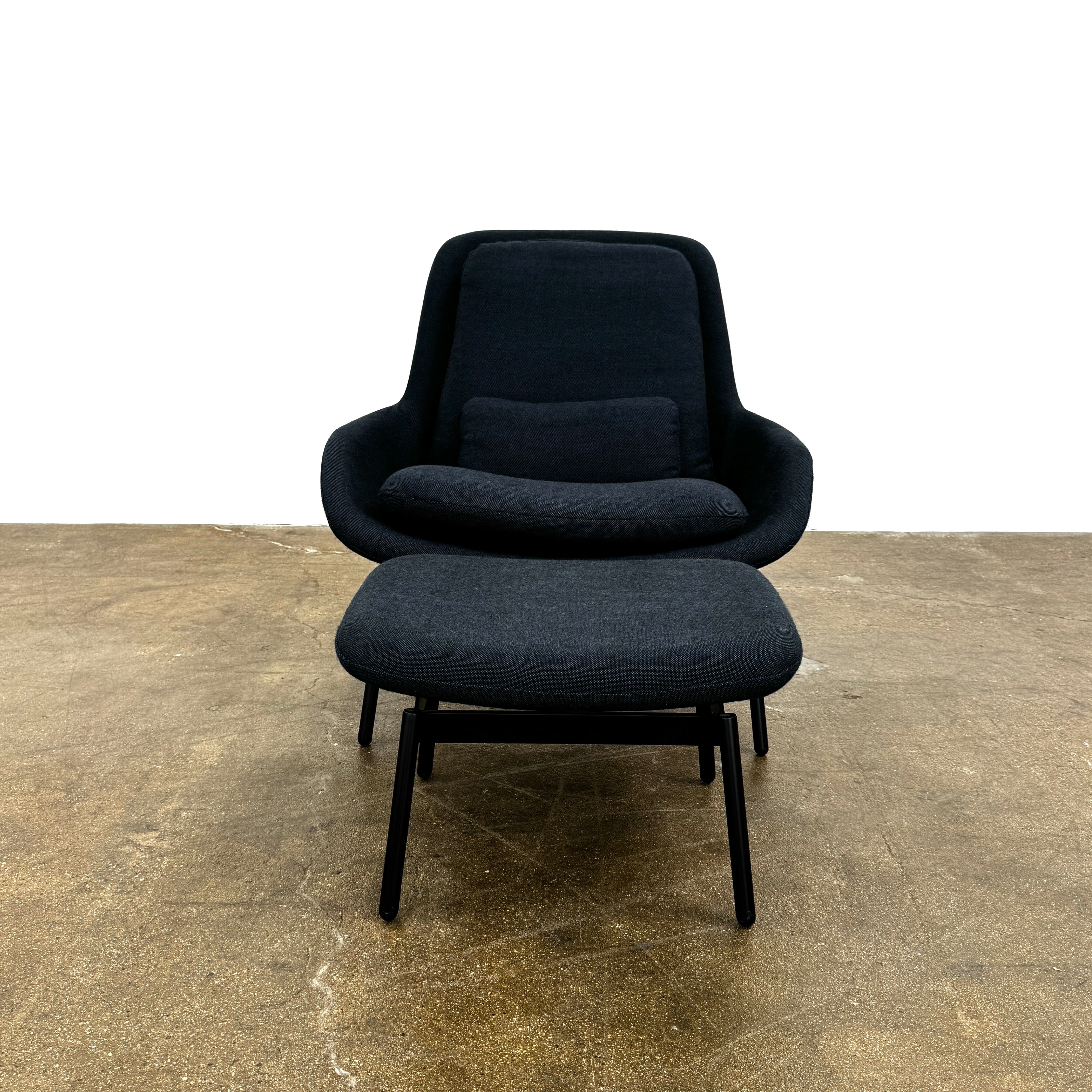 A Bludot Field Chair & Ottoman by Blu Dot, in modern black, is placed on a brown concrete floor with a white background.