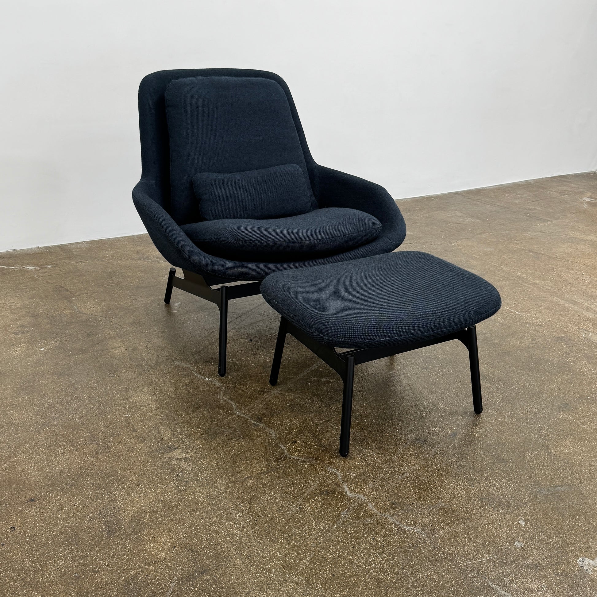 A Bludot Field Chair & Ottoman by Blu Dot, in modern black, is placed on a brown concrete floor with a white background.