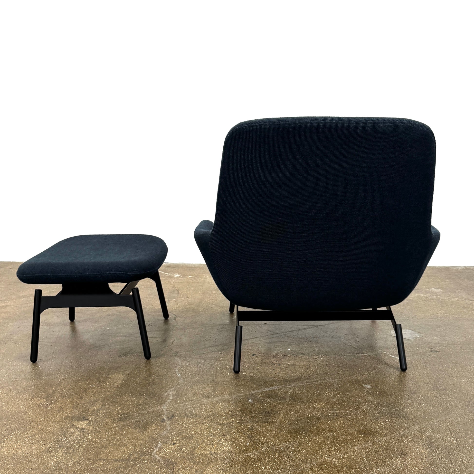 A Bludot Field Chair & Ottoman by Blu Dot, in modern black, is placed on a brown concrete floor with a white background.