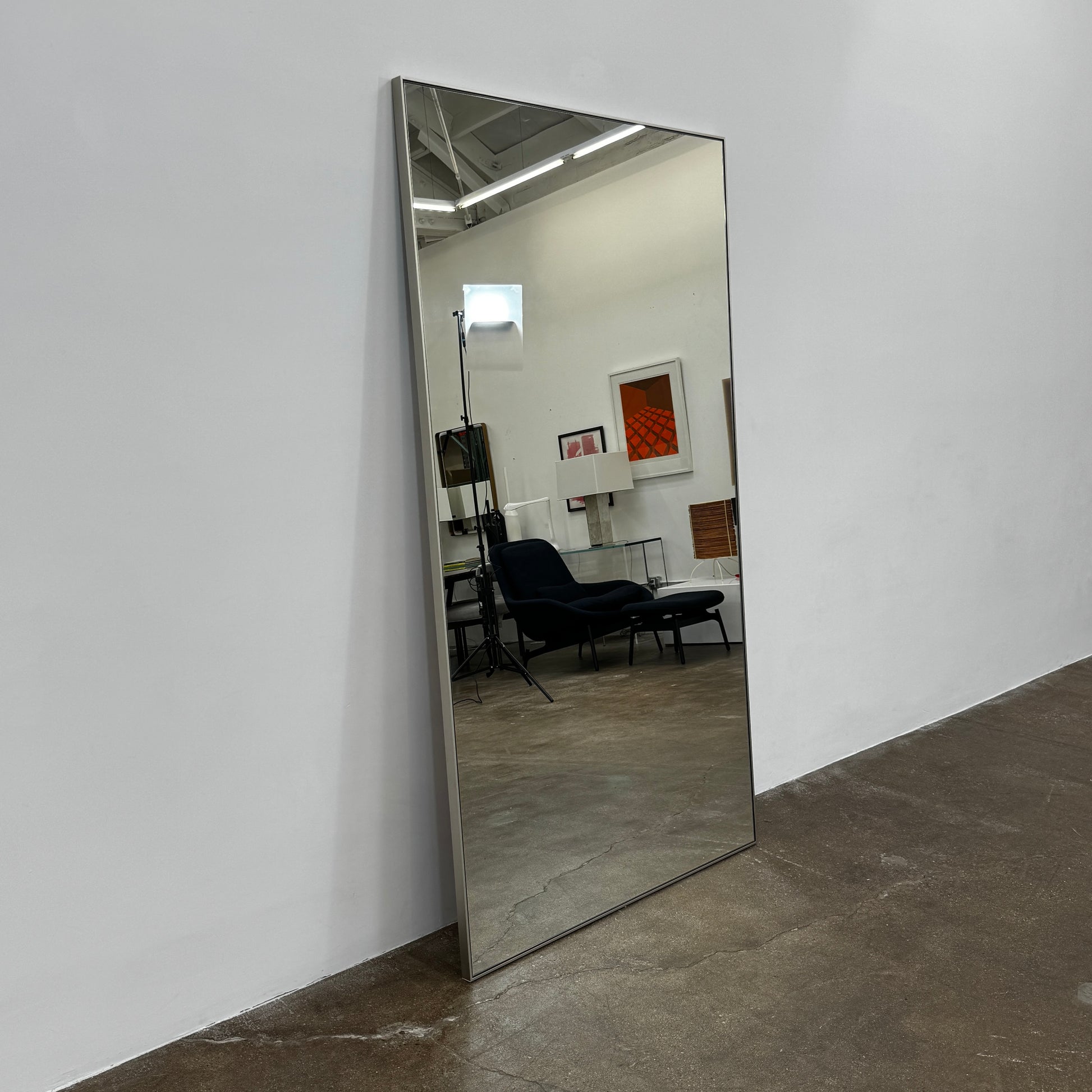 The DWR Mondrian Wall Hanging Mirror (44" x 80") by DWR features a sleek, minimalist rectangular design with a thin, dark frame and stands upright against a plain white backdrop for a modern look.