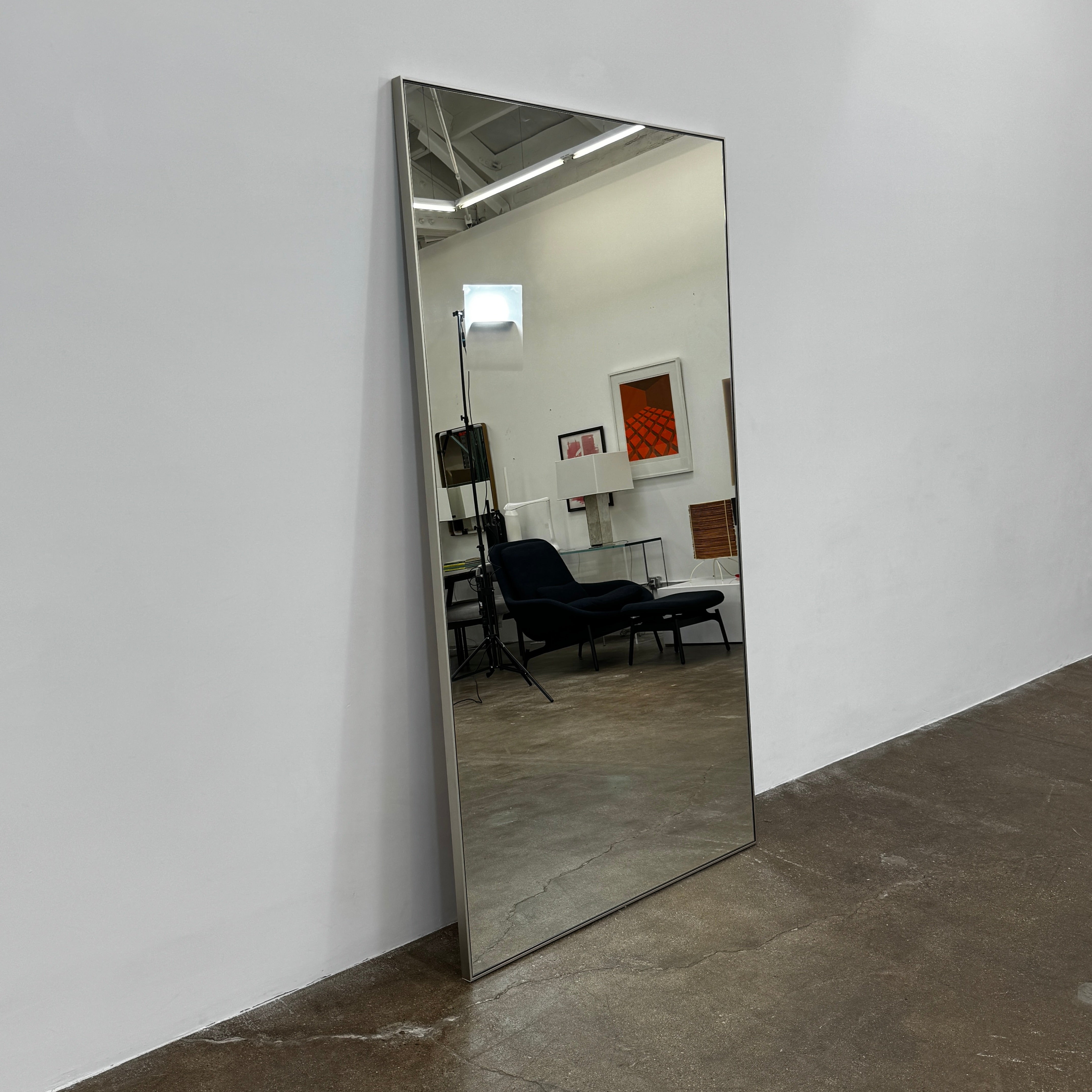 The DWR Mondrian Wall Hanging Mirror (44" x 80") by DWR features a sleek, minimalist rectangular design with a thin, dark frame and stands upright against a plain white backdrop for a modern look.