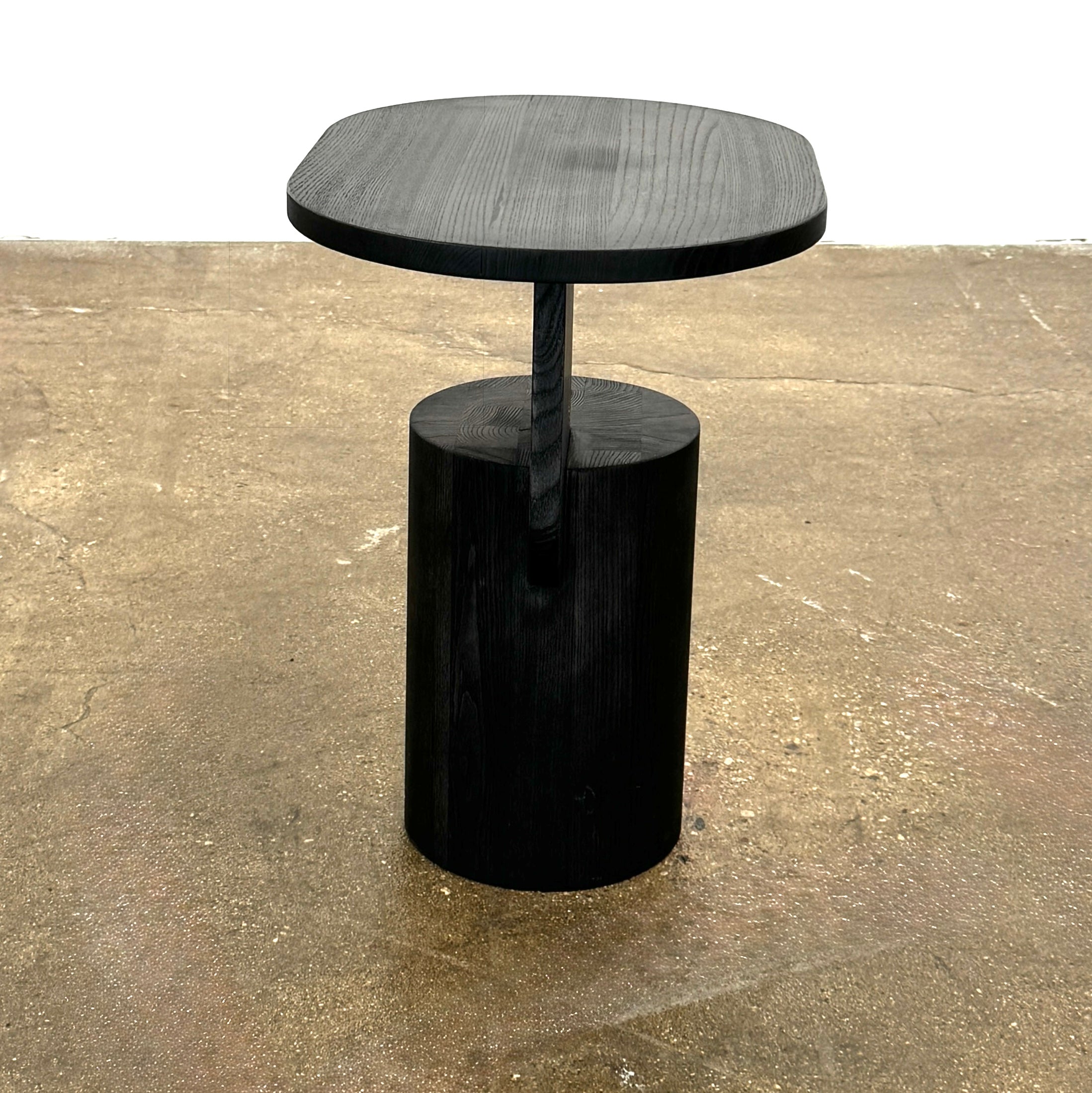 The Ferm Living Insert Side Table by Ferm Living features an oval dark wood top with a pedestal base, creating a striking accent on concrete floors and showcasing subtle Scandinavian design.