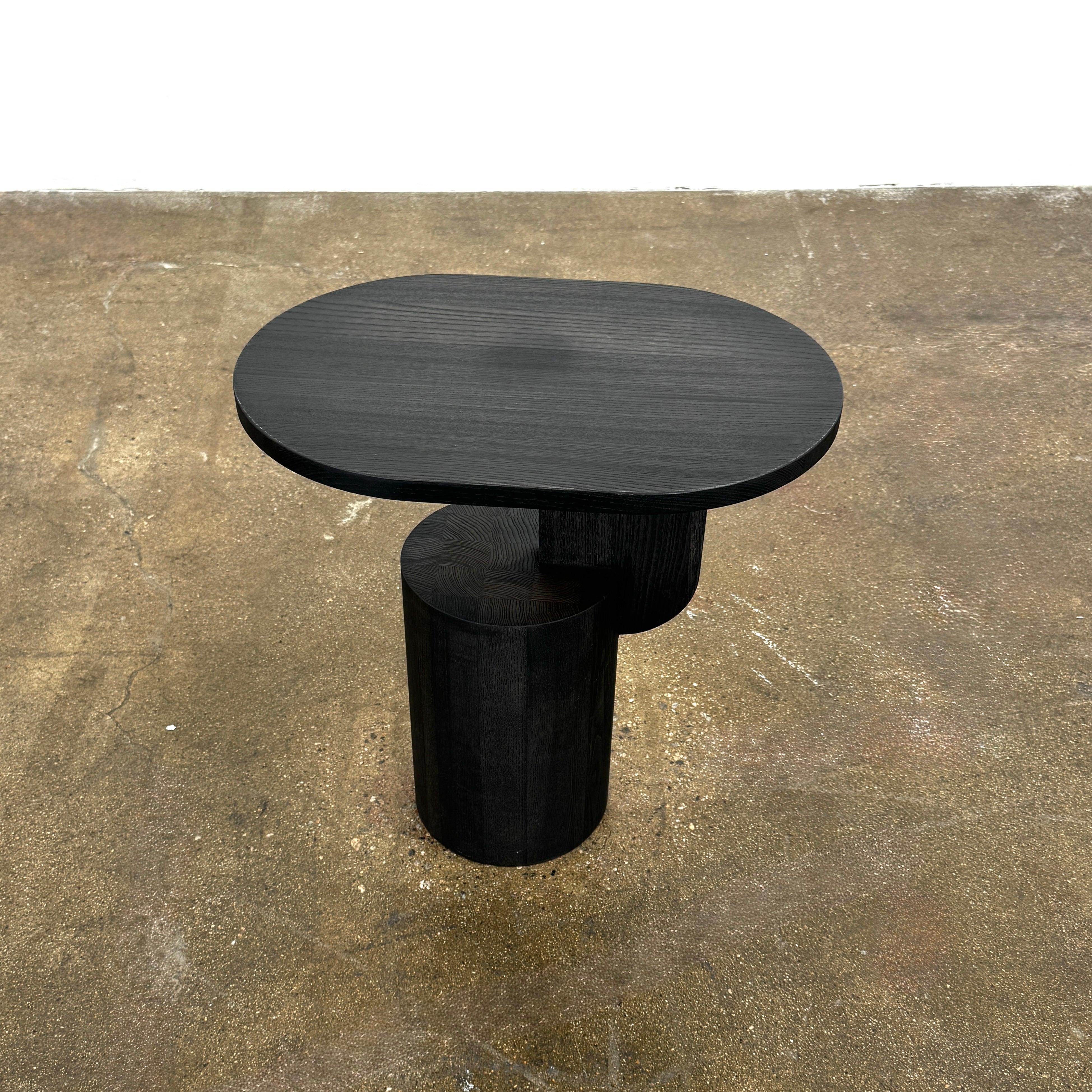 The Ferm Living Insert Side Table by Ferm Living features an oval dark wood top with a pedestal base, creating a striking accent on concrete floors and showcasing subtle Scandinavian design.