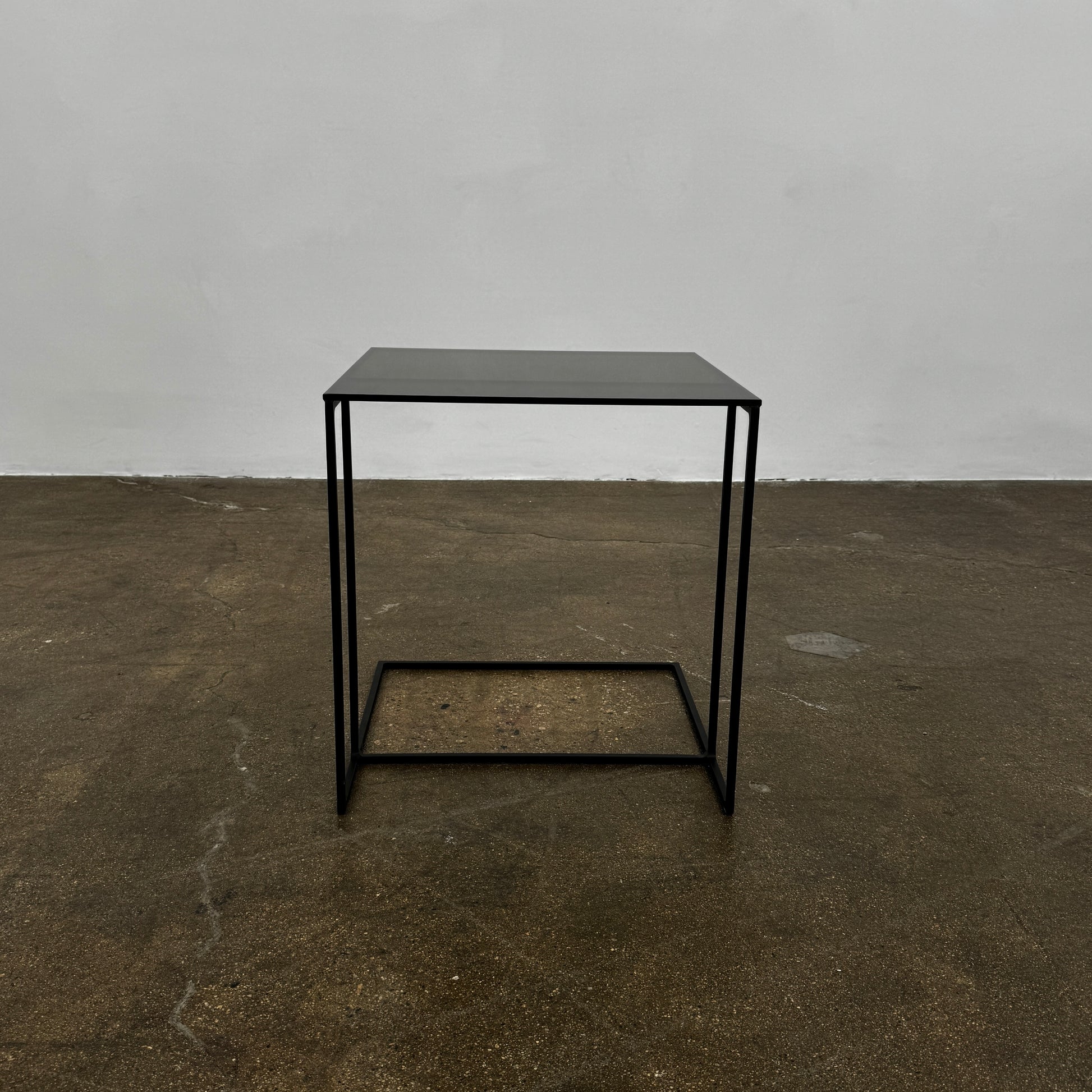 The Minotti Leger accent table by Minotti features a minimalist black metal frame with geometric lines and a flat rectangular bronze glass top, inspired by the cantilever style, shown against a plain background.