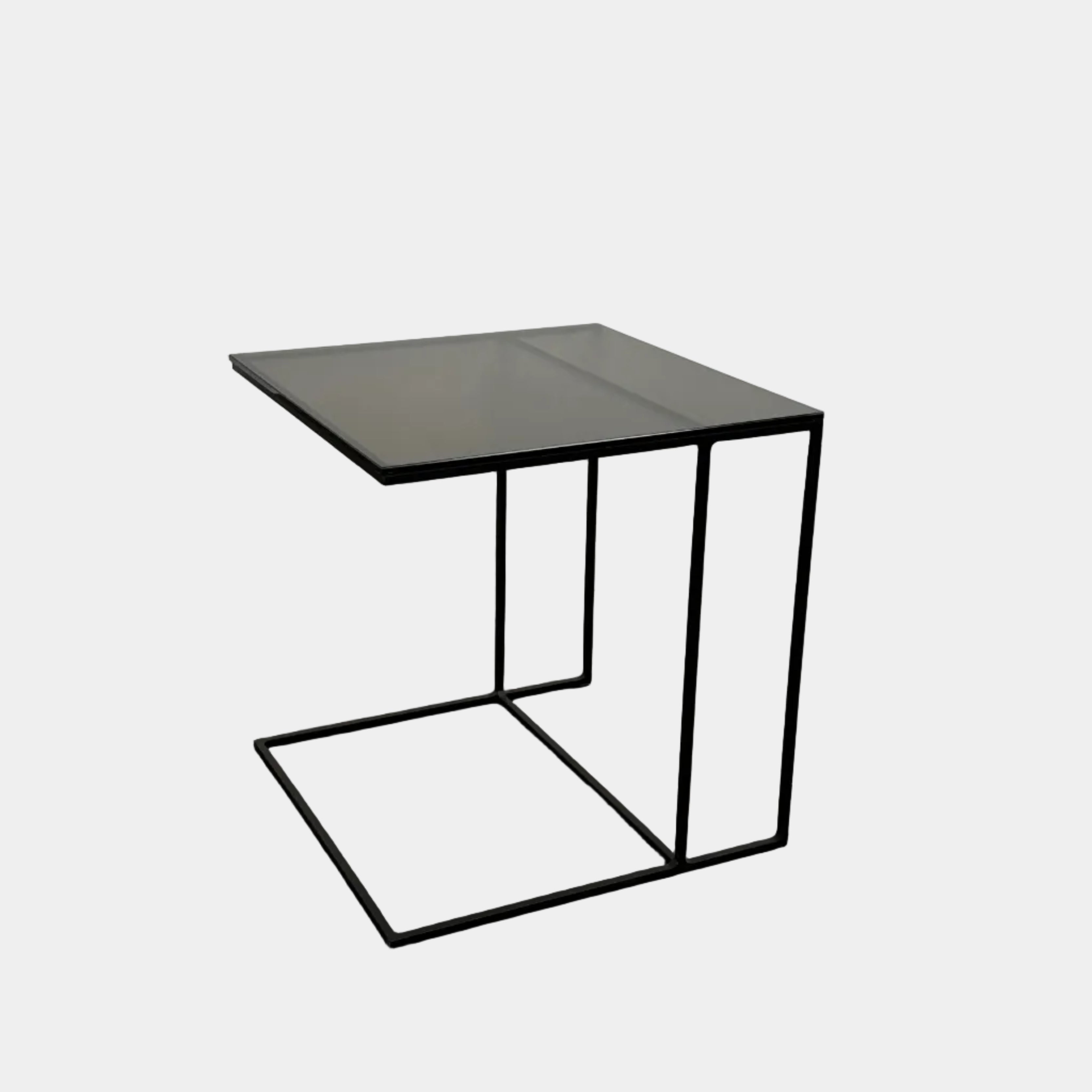 The Minotti Leger accent table by Minotti features a minimalist black metal frame with geometric lines and a flat rectangular bronze glass top, inspired by the cantilever style, shown against a plain background.