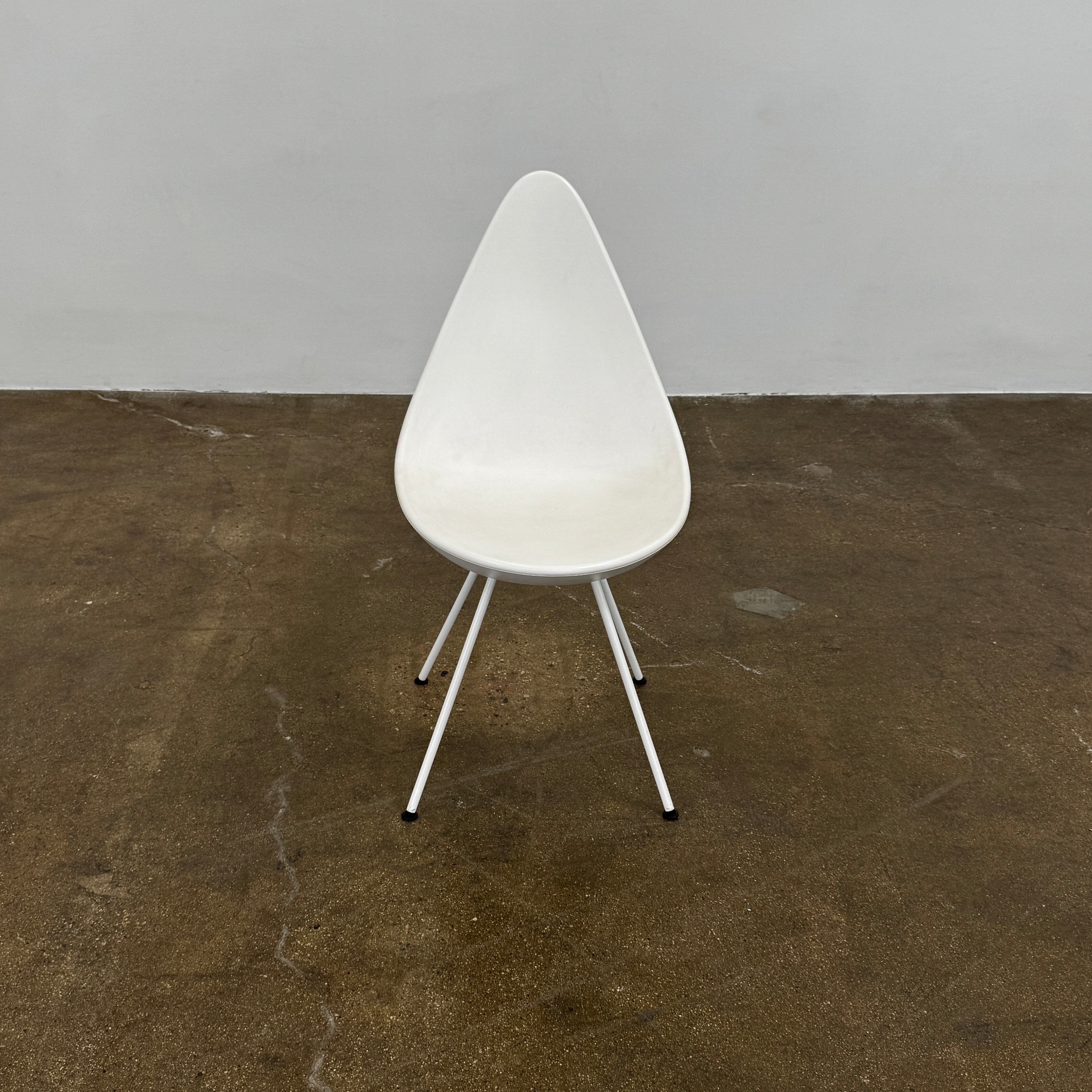 The Fritz Hansen Drop Chair Set of 4 by Fritz Hansen features white modernist chairs with teardrop-shaped backs and slender metal legs, inspired by the iconic Arne Jacobsen design, arranged in a staggered formation on a plain background.