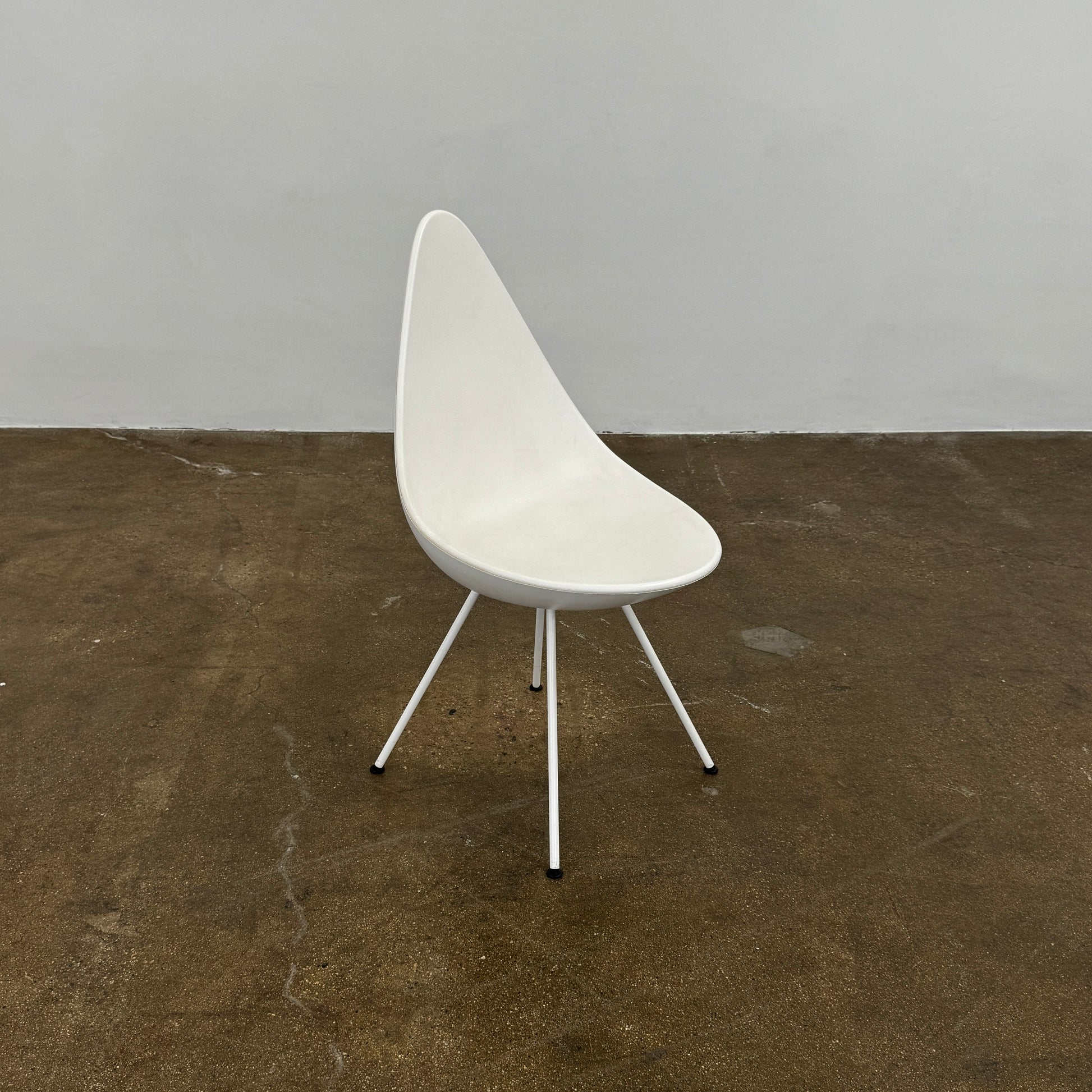 The Fritz Hansen Drop Chair Set of 4 by Fritz Hansen features white modernist chairs with teardrop-shaped backs and slender metal legs, inspired by the iconic Arne Jacobsen design, arranged in a staggered formation on a plain background.