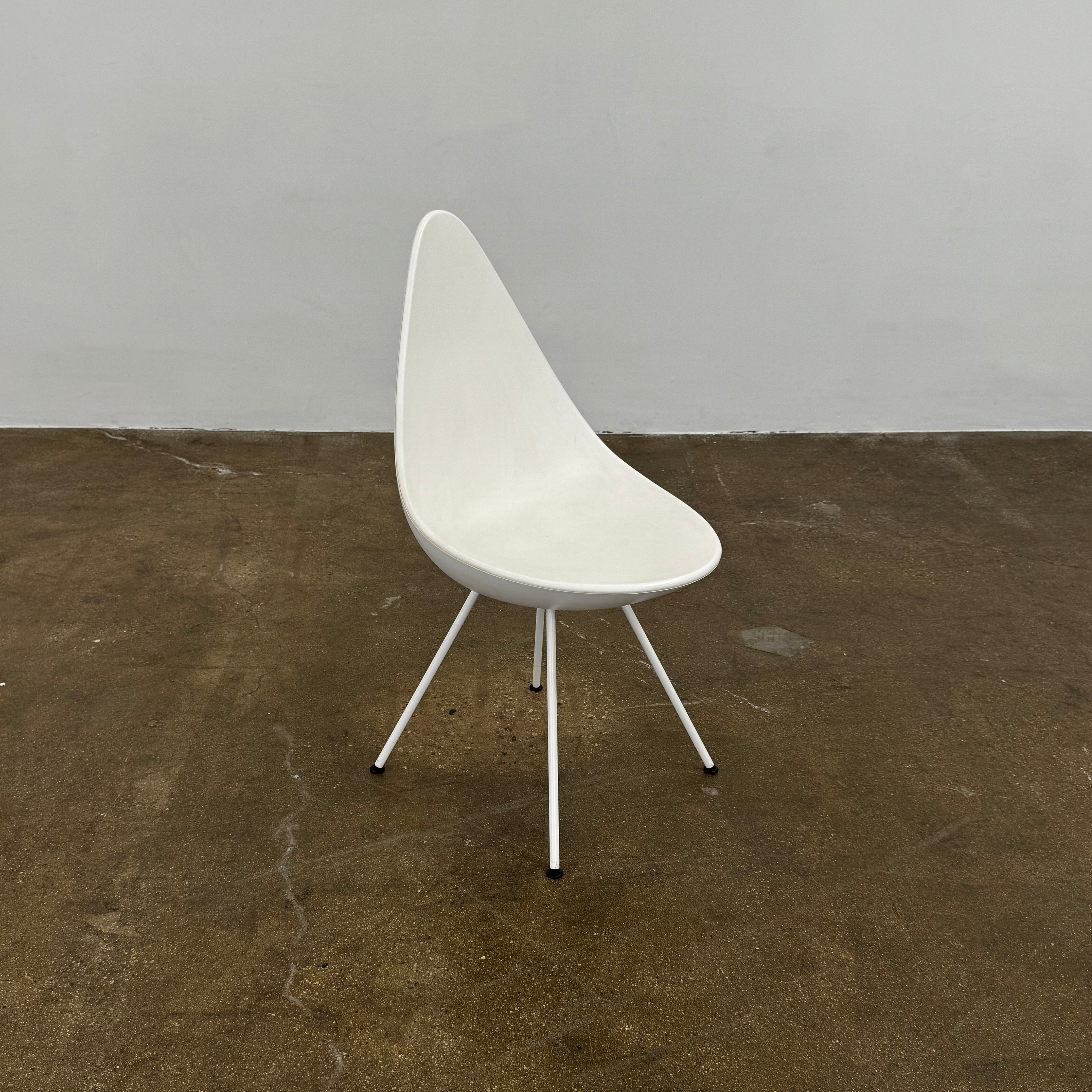 The Fritz Hansen Drop Chair Set of 4 by Fritz Hansen features white modernist chairs with teardrop-shaped backs and slender metal legs, inspired by the iconic Arne Jacobsen design, arranged in a staggered formation on a plain background.