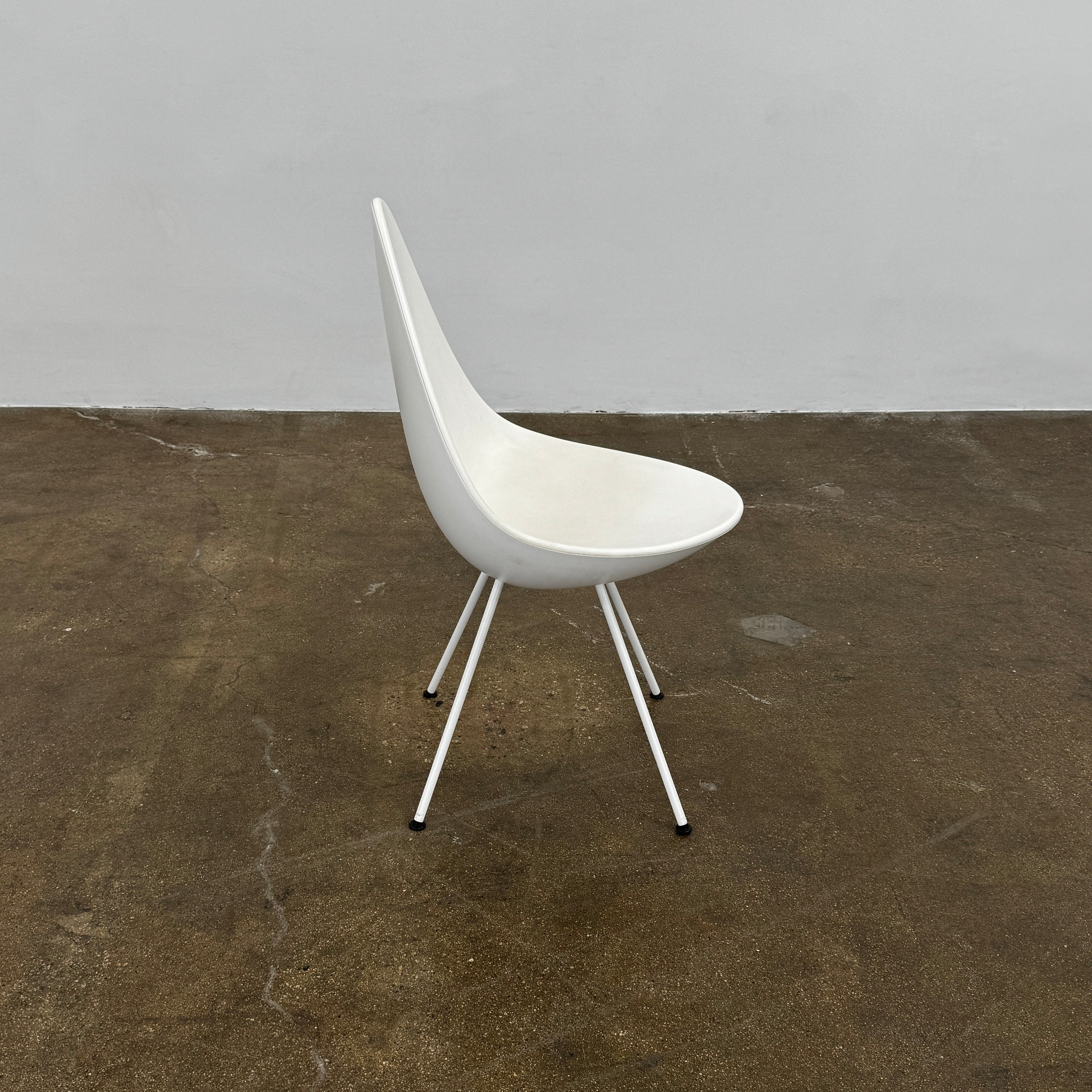 The Fritz Hansen Drop Chair Set of 4 by Fritz Hansen features white modernist chairs with teardrop-shaped backs and slender metal legs, inspired by the iconic Arne Jacobsen design, arranged in a staggered formation on a plain background.