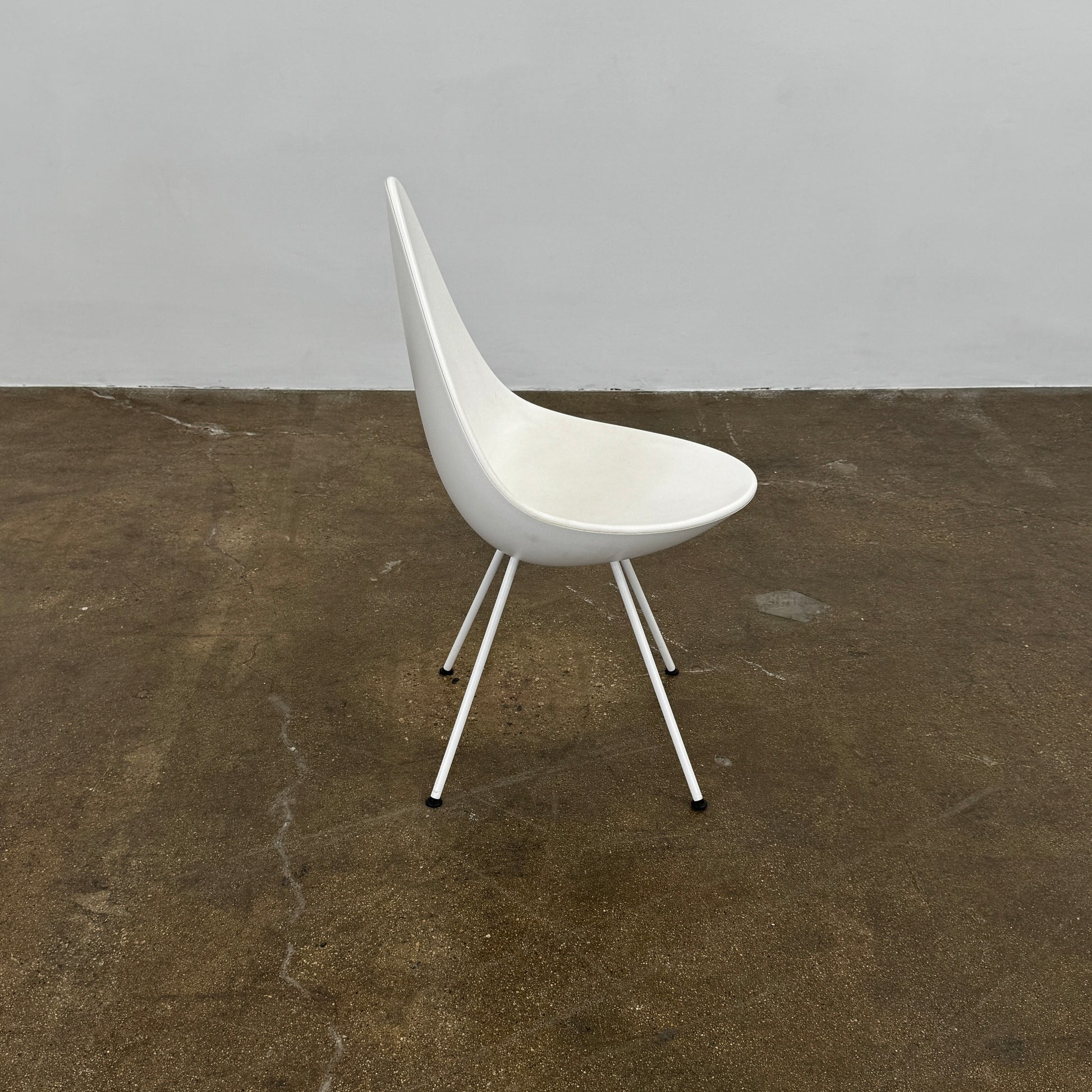 The Fritz Hansen Drop Chair Set of 4 by Fritz Hansen features white modernist chairs with teardrop-shaped backs and slender metal legs, inspired by the iconic Arne Jacobsen design, arranged in a staggered formation on a plain background.