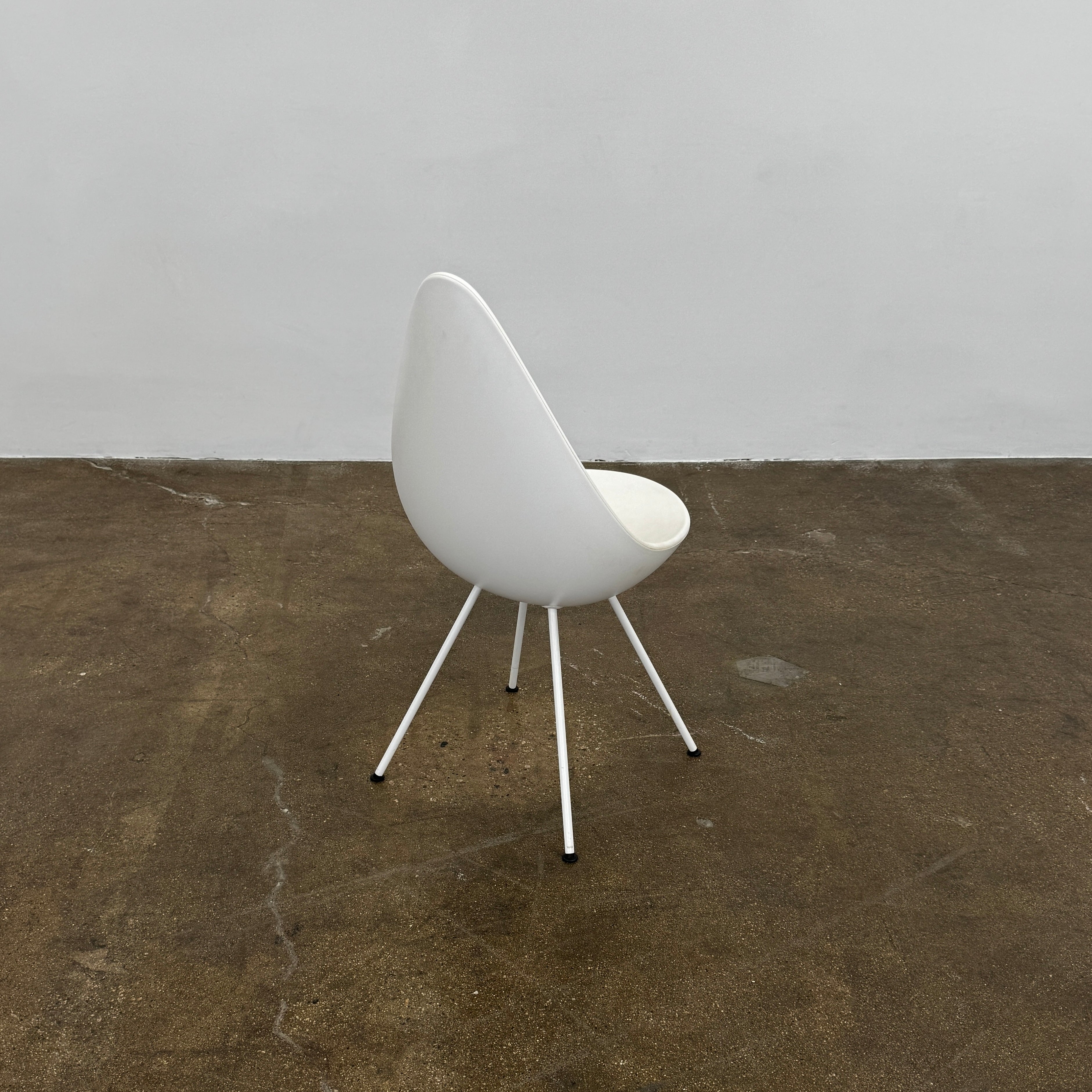 The Fritz Hansen Drop Chair Set of 4 by Fritz Hansen features white modernist chairs with teardrop-shaped backs and slender metal legs, inspired by the iconic Arne Jacobsen design, arranged in a staggered formation on a plain background.