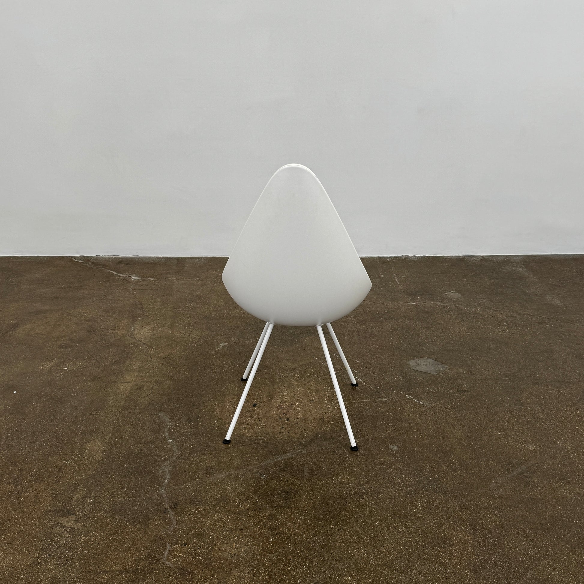 The Fritz Hansen Drop Chair Set of 4 by Fritz Hansen features white modernist chairs with teardrop-shaped backs and slender metal legs, inspired by the iconic Arne Jacobsen design, arranged in a staggered formation on a plain background.