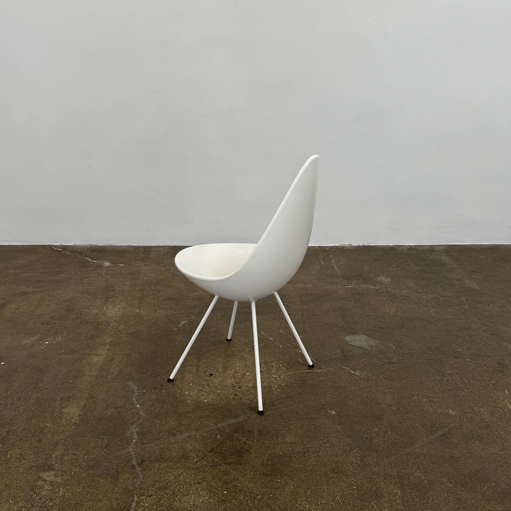 The Fritz Hansen Drop Chair Set of 4 by Fritz Hansen features white modernist chairs with teardrop-shaped backs and slender metal legs, inspired by the iconic Arne Jacobsen design, arranged in a staggered formation on a plain background.
