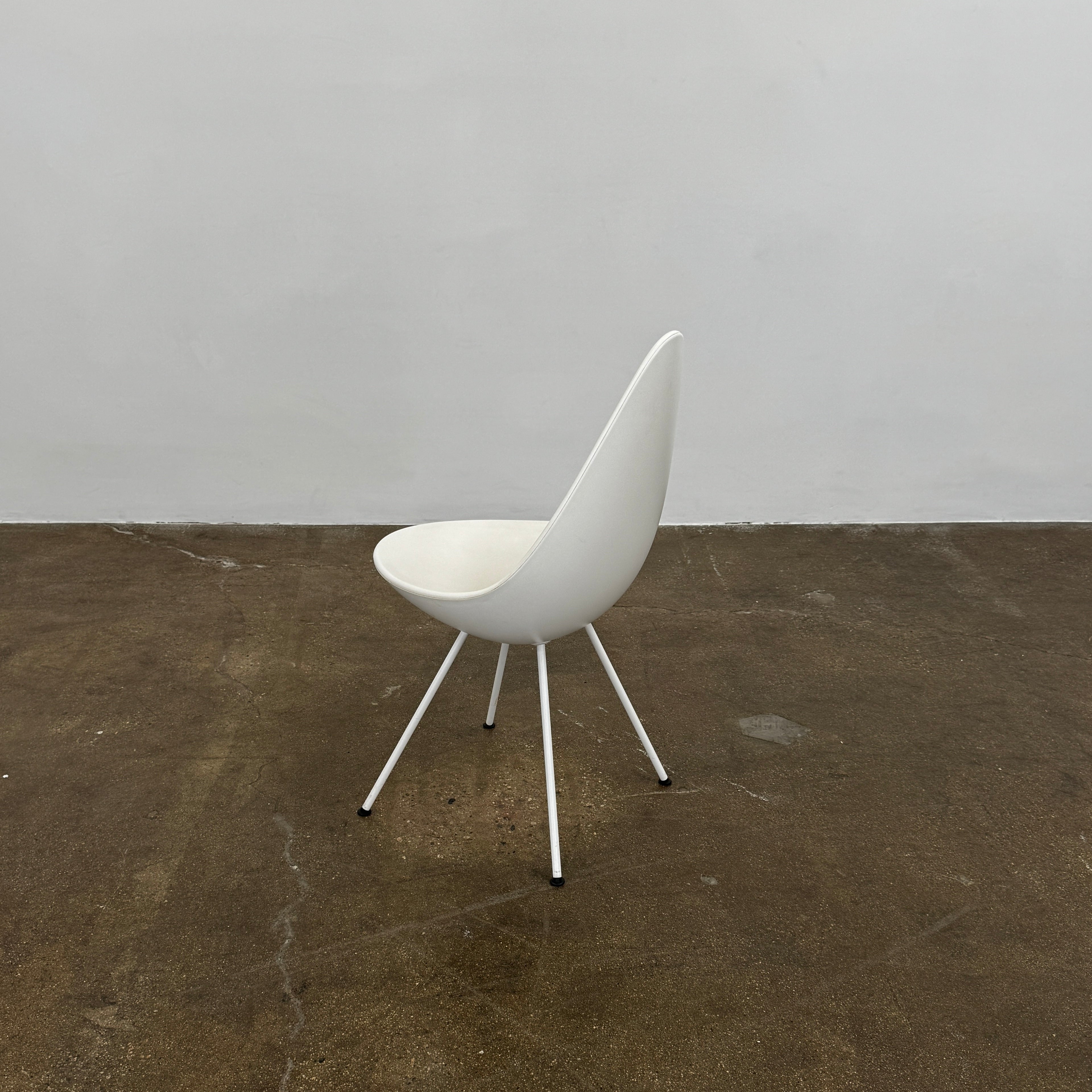 The Fritz Hansen Drop Chair Set of 4 by Fritz Hansen features white modernist chairs with teardrop-shaped backs and slender metal legs, inspired by the iconic Arne Jacobsen design, arranged in a staggered formation on a plain background.