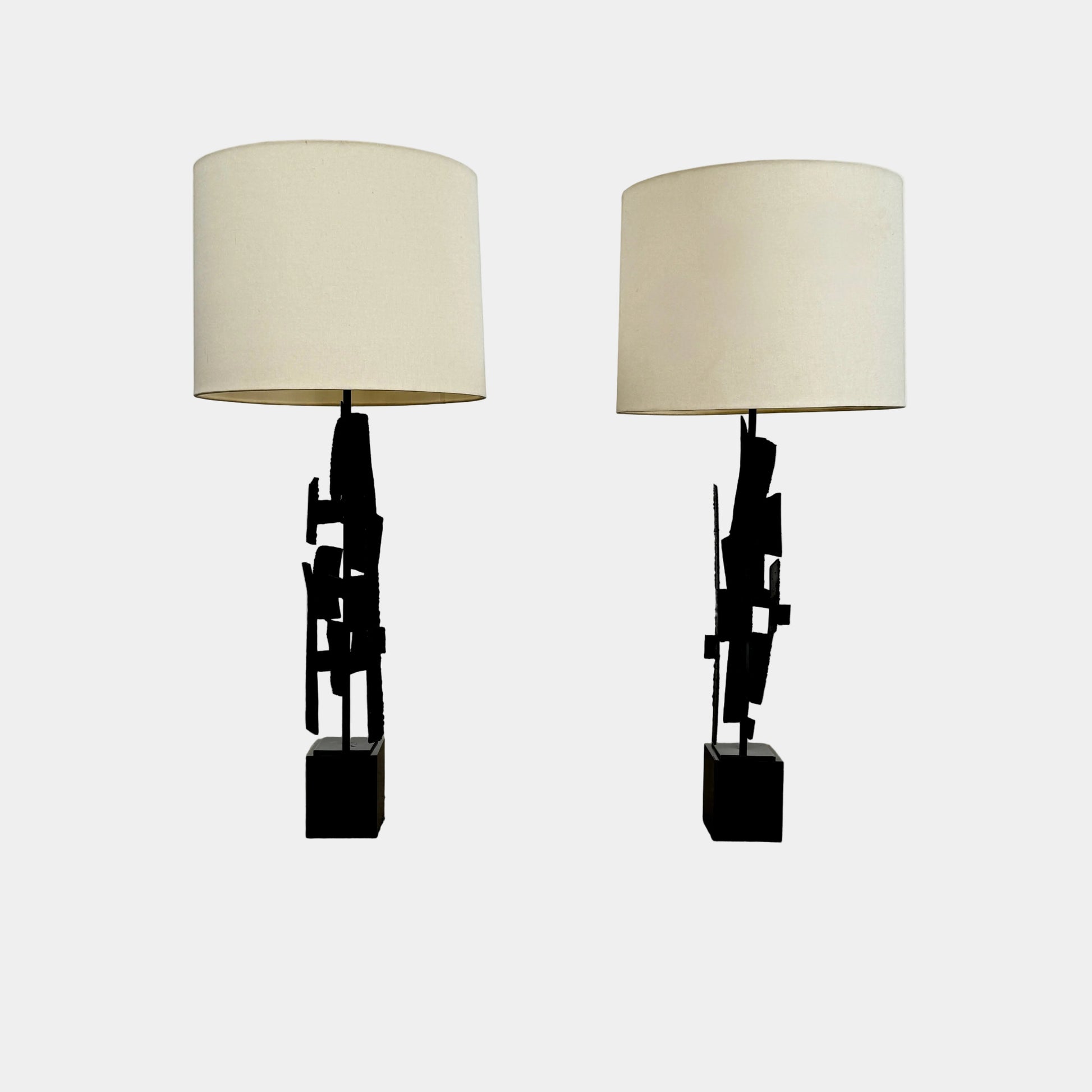 A pair of Vintage Richard Barr Iron Brutalist table lamps for Laurel Lamp Co., featuring abstract black metal bases and cylindrical white shades, set against a plain white background.