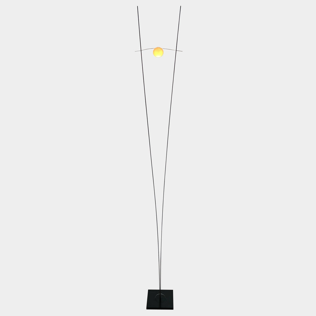 An Ingo Maurer Ilios Floor Light with two metal poles and a yellow bulb.