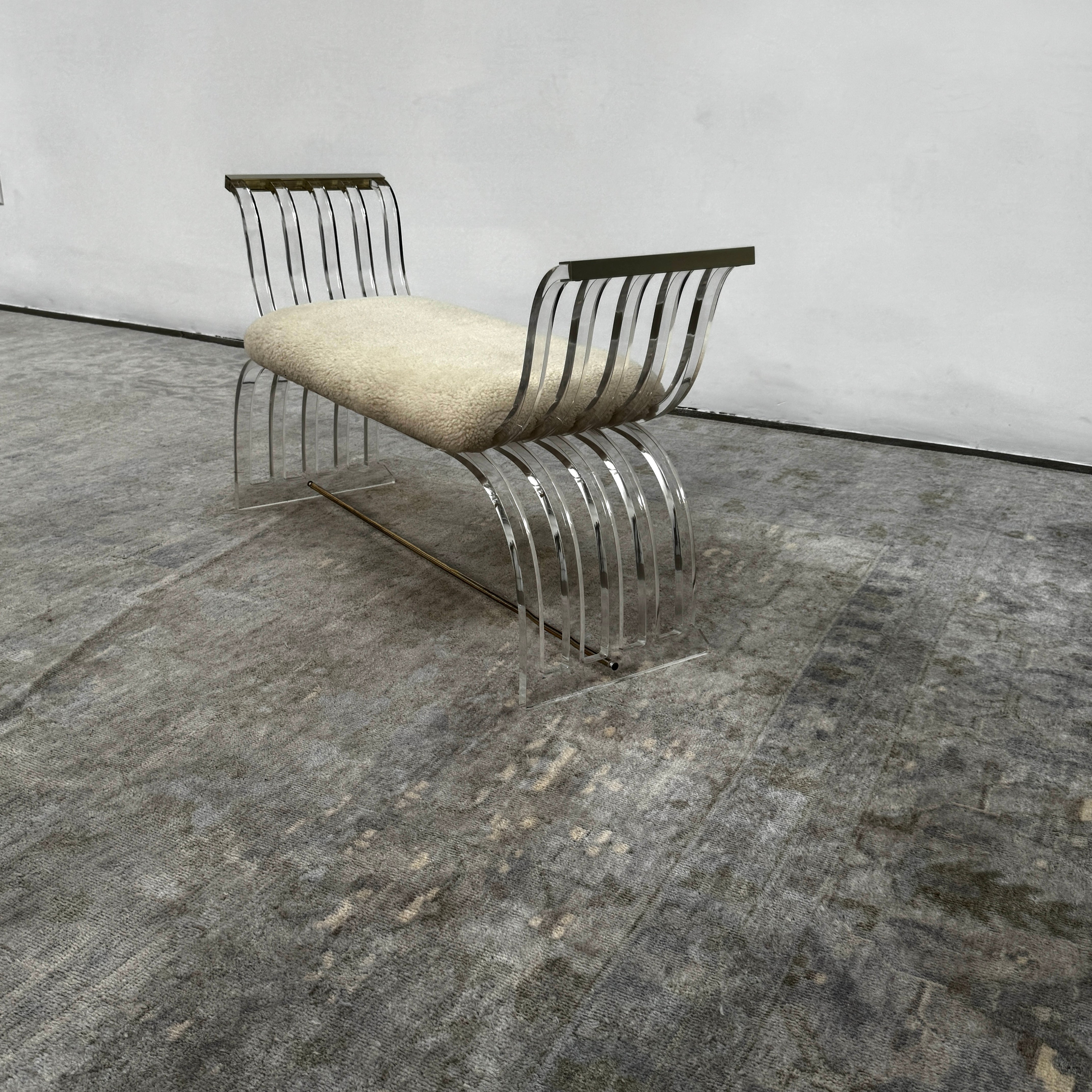 The Vintage Charles Hollis Jones Lucite Bench features a transparent acrylic frame, curved armrests, and a rectangular beige shearling cushion, shown against a plain white background.