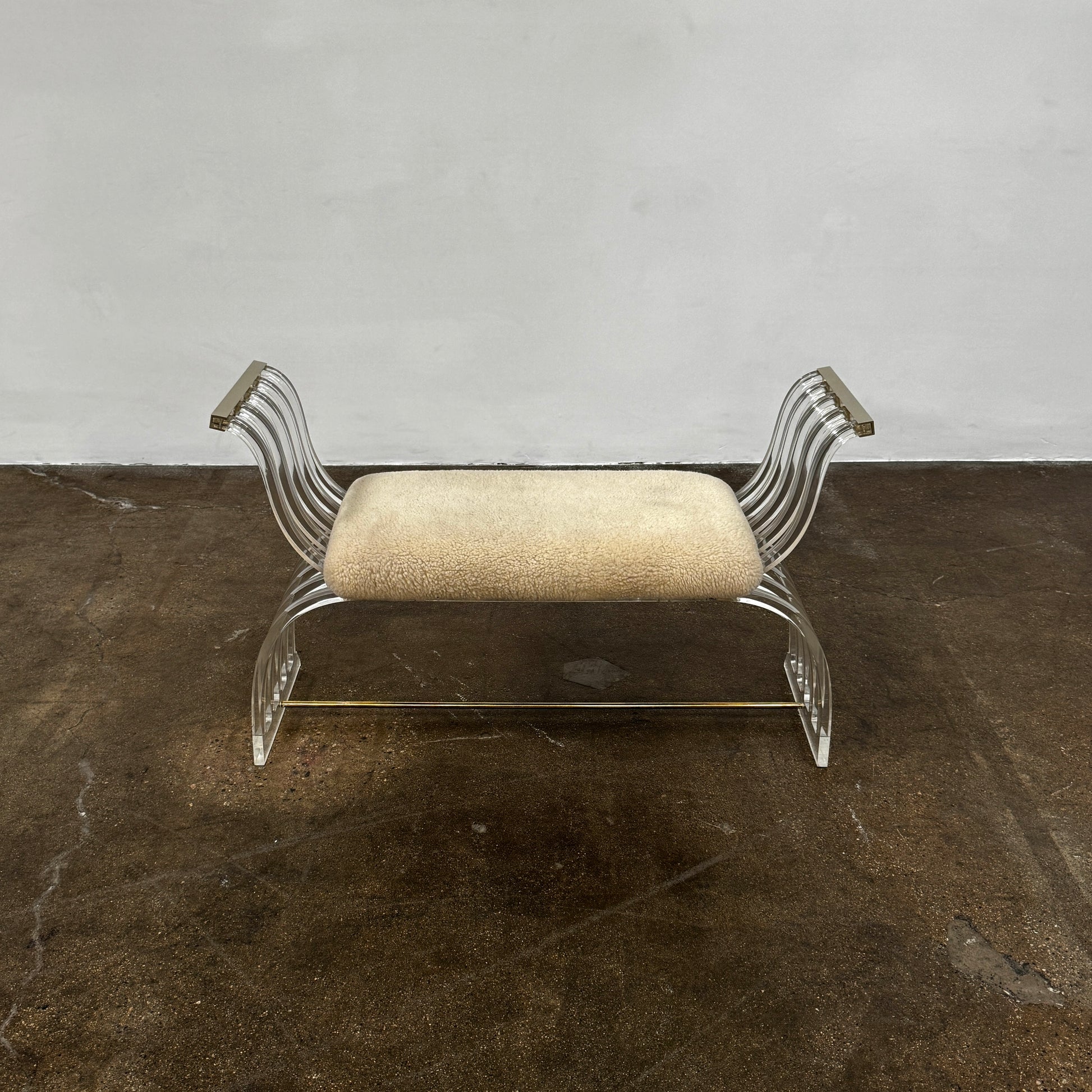The Vintage Charles Hollis Jones Lucite Bench features a transparent acrylic frame, curved armrests, and a rectangular beige shearling cushion, shown against a plain white background.
