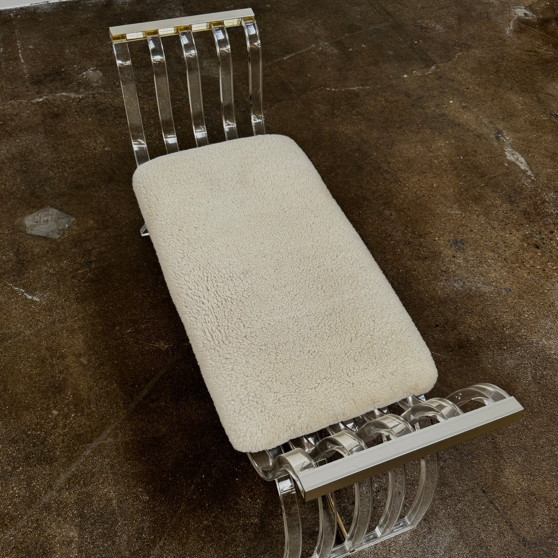 The Vintage Charles Hollis Jones Lucite Bench features a transparent acrylic frame, curved armrests, and a rectangular beige shearling cushion, shown against a plain white background.