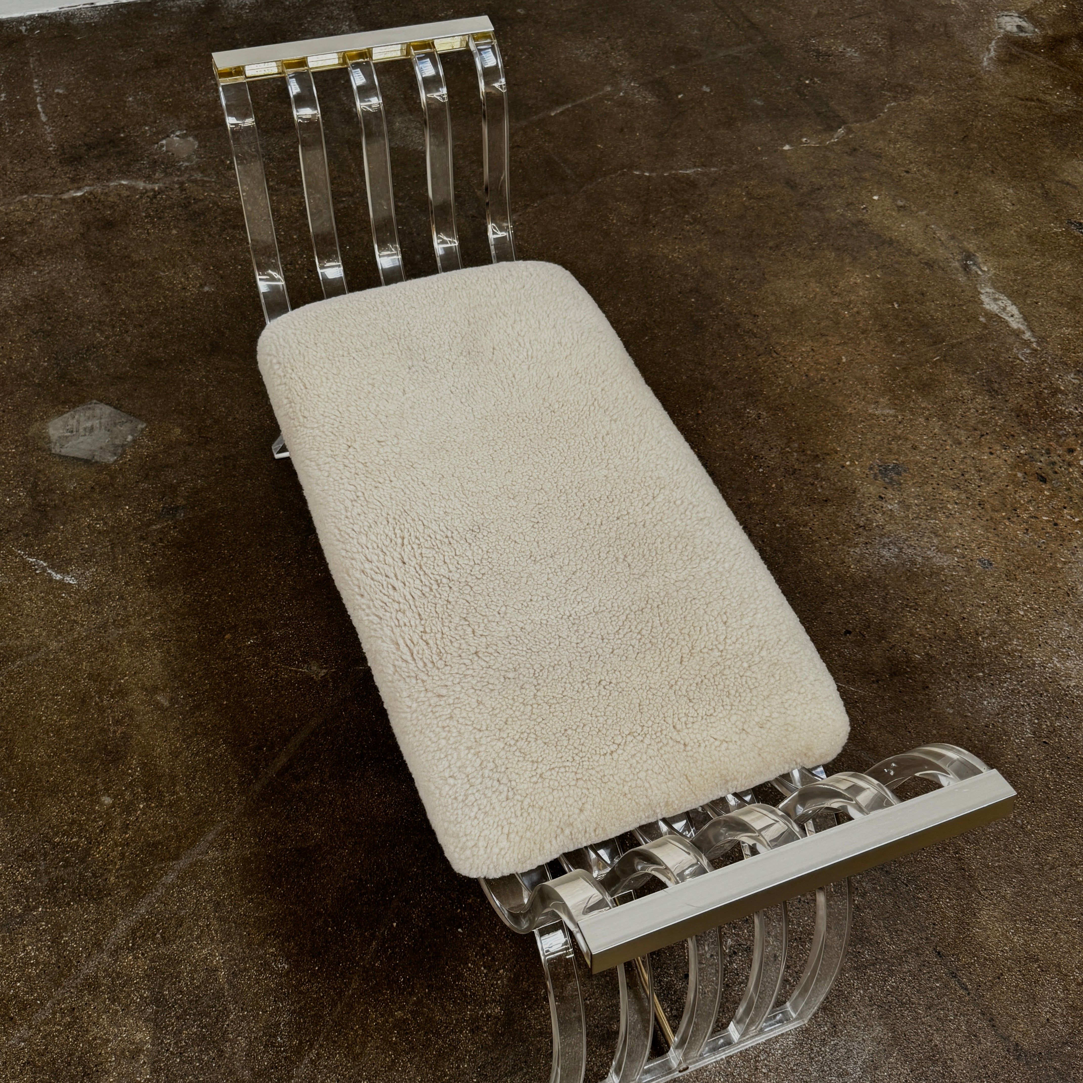 The Vintage Charles Hollis Jones Lucite Bench features a transparent acrylic frame, curved armrests, and a rectangular beige shearling cushion, shown against a plain white background.