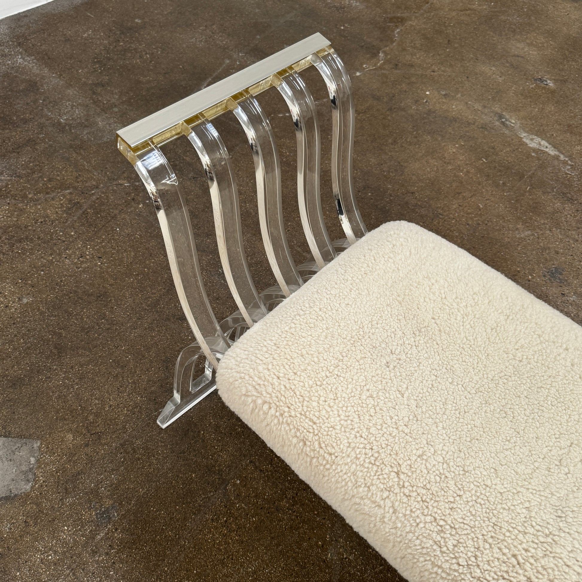 The Vintage Charles Hollis Jones Lucite Bench features a transparent acrylic frame, curved armrests, and a rectangular beige shearling cushion, shown against a plain white background.