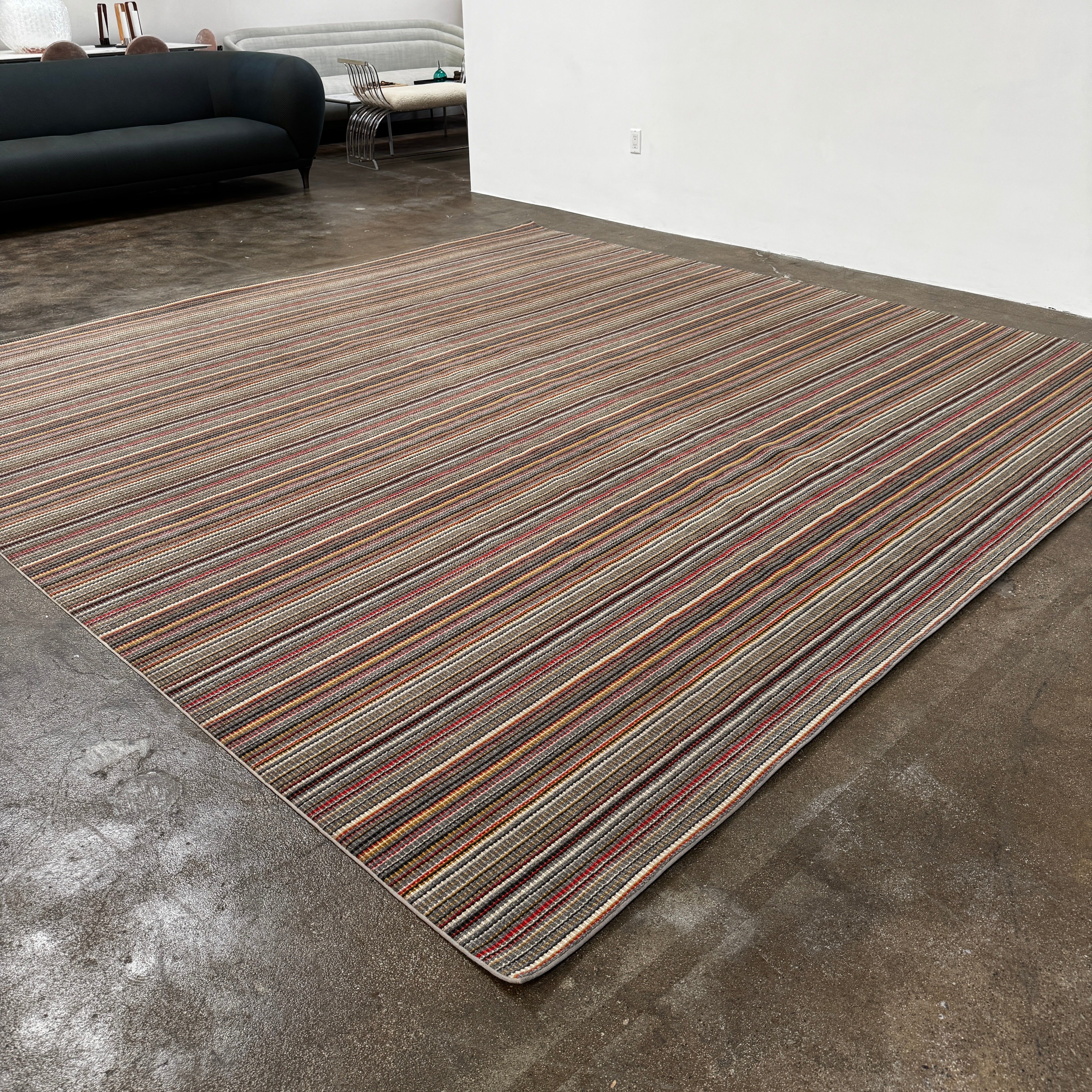 A close-up of the Maharam Interval Area Rug by Herman Miller, a modern New Zealand wool rug featuring gray, red, yellow, white, and brown stripes, shown on a white background.