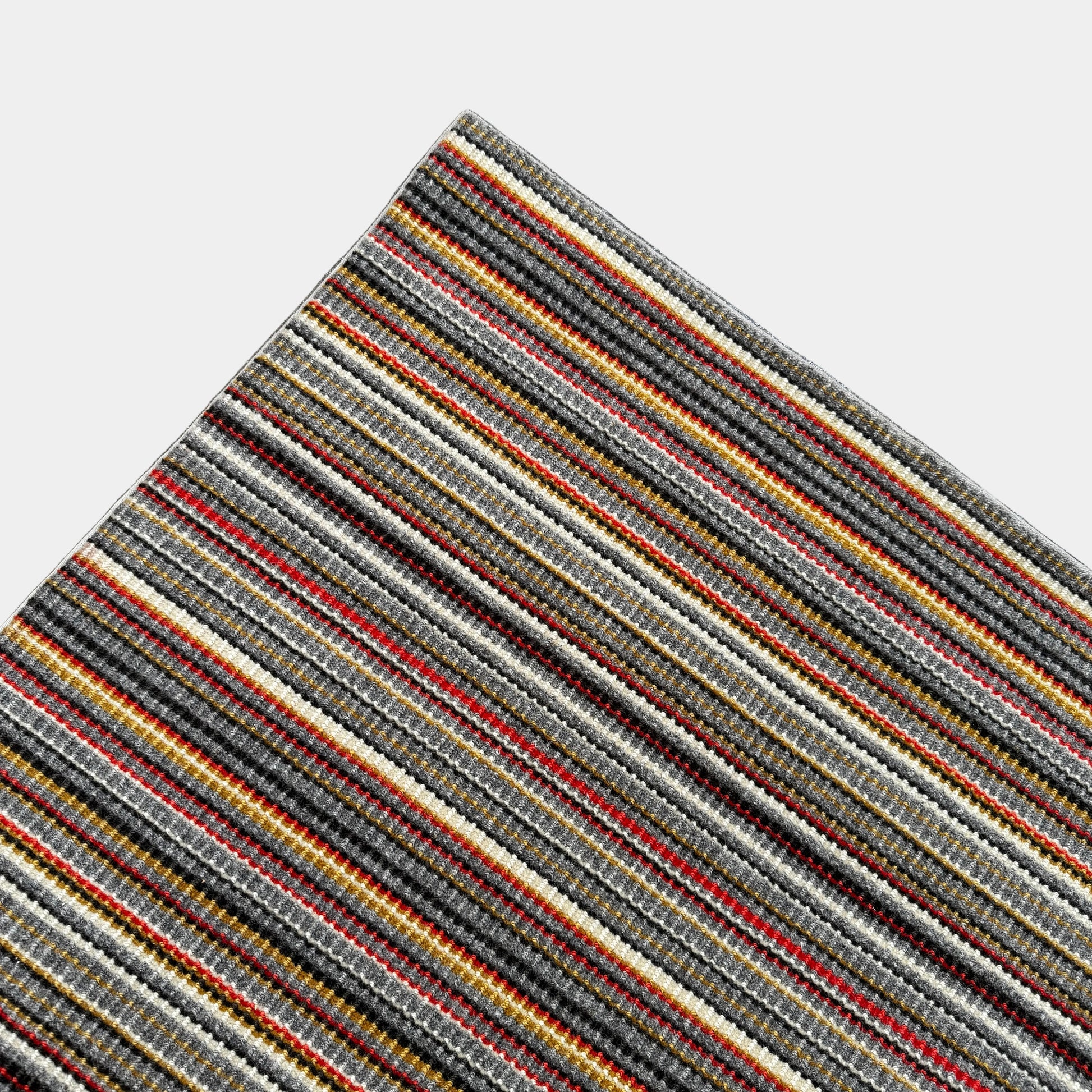A close-up of the Maharam Interval Area Rug by Herman Miller, a modern New Zealand wool rug featuring gray, red, yellow, white, and brown stripes, shown on a white background.