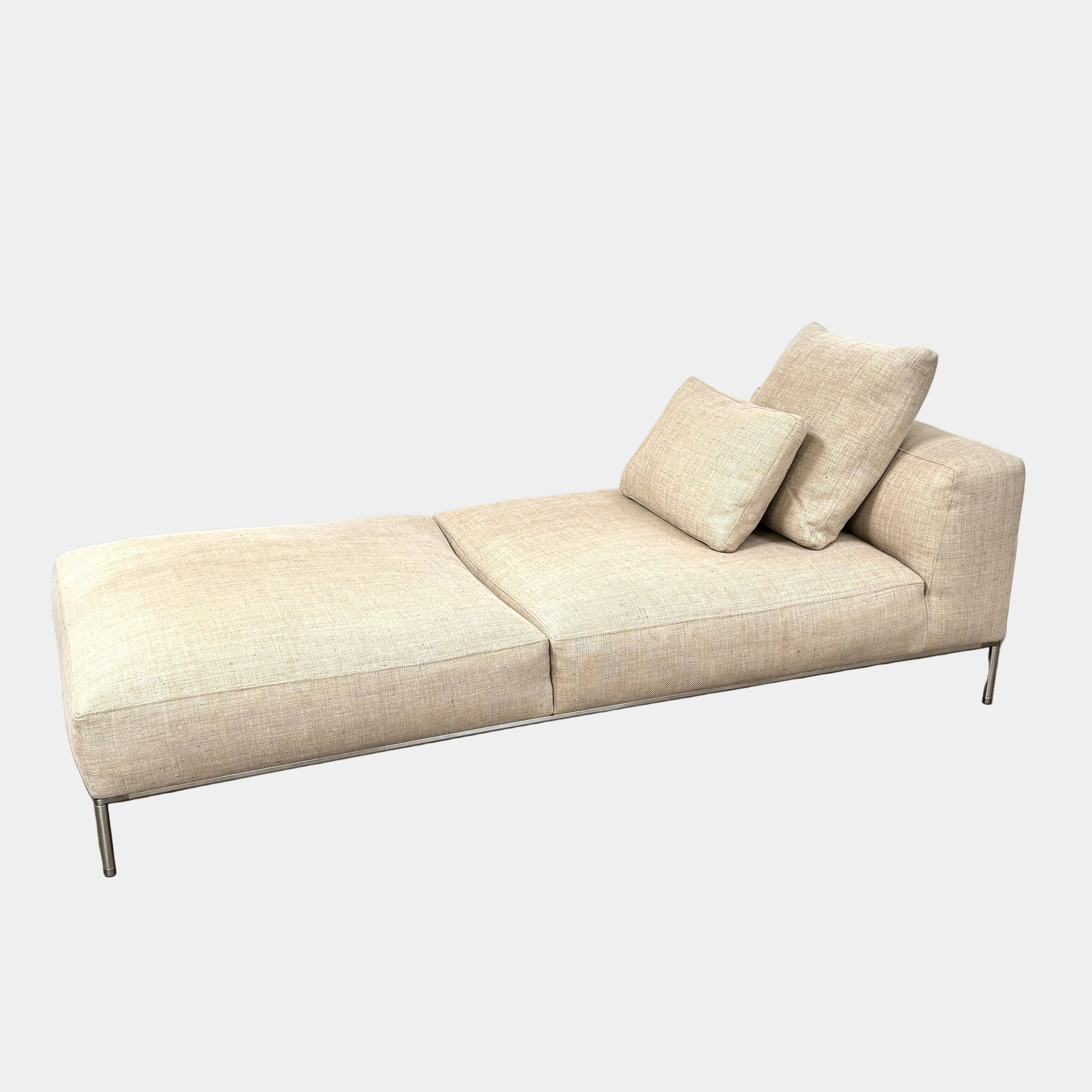 The B&B Italia Frank Chaise Lounge, upholstered in light beige with two matching cushions and metal legs, is showcased against a plain white background.