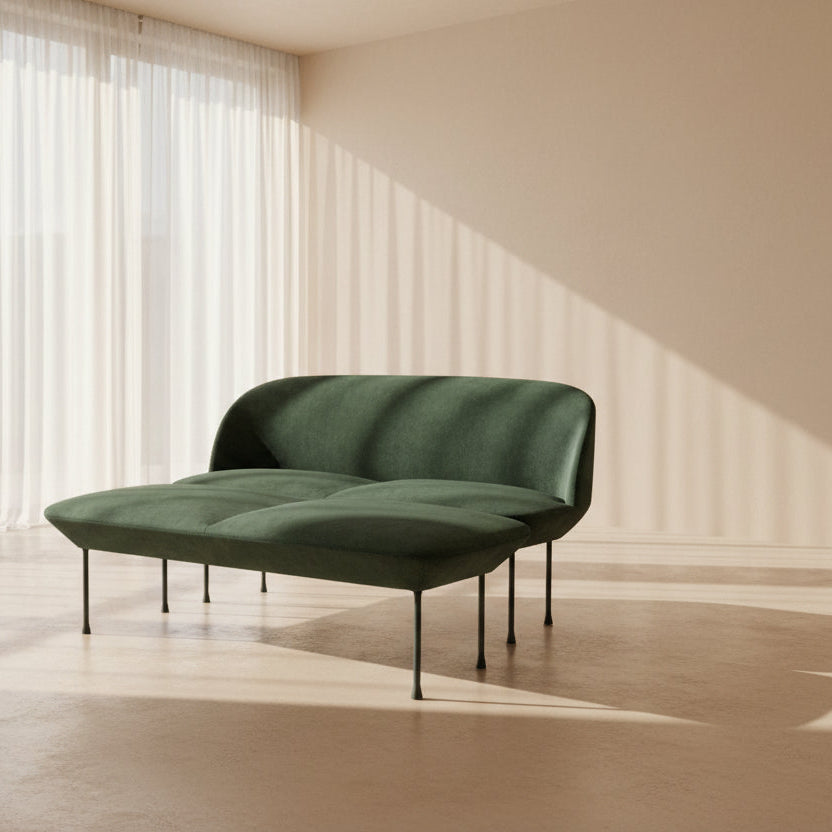 The Muuto Oslo 2-seat sofa & bench by Muuto, featuring modern green upholstery and slim black legs inspired by Danish design, stands in a bright room with beige walls and sheer white curtains.