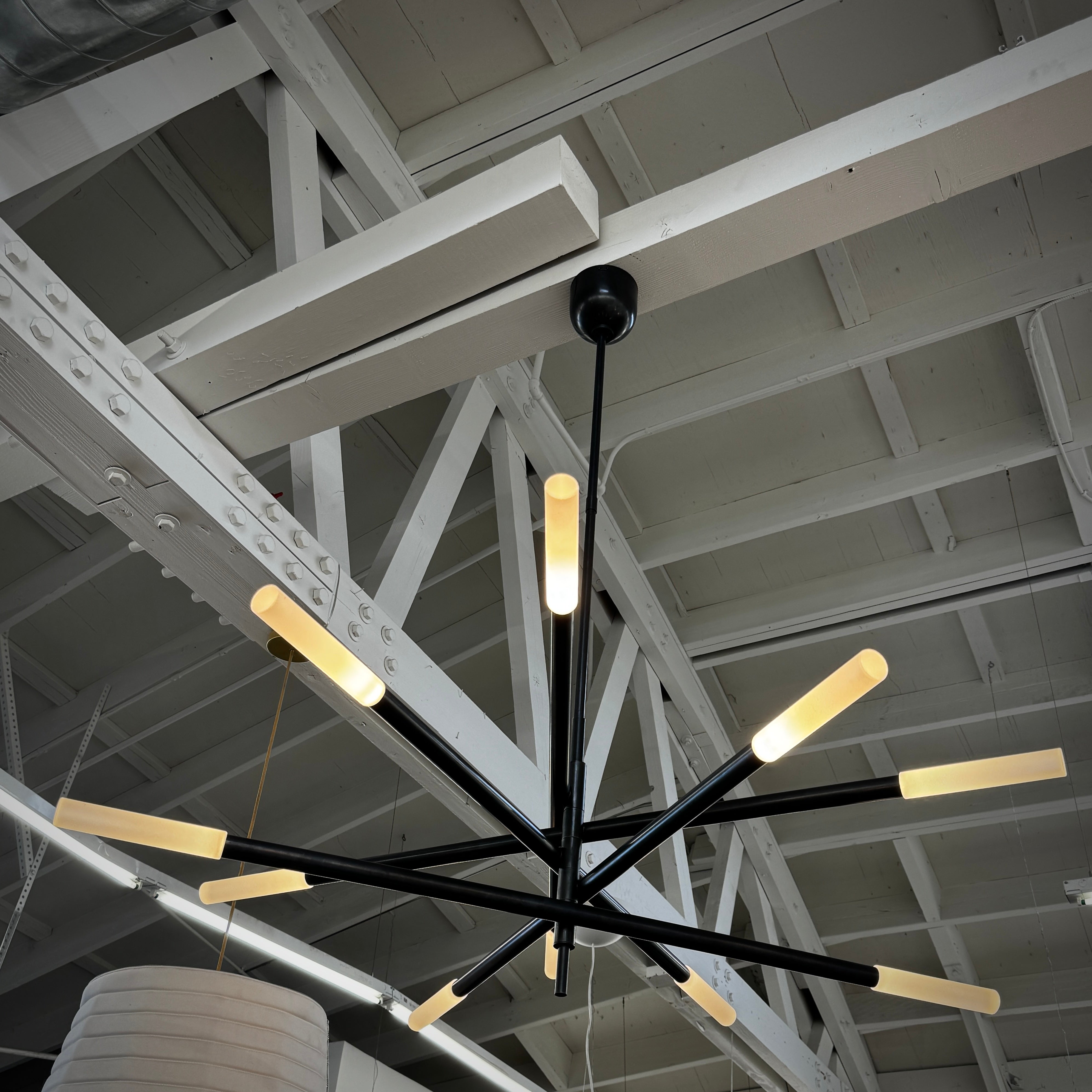 The Visual Comfort Signature Rousseau Grande Ten Light Articulating Chandelier features a modern black design with ten horizontal arms, each ending in a yellow-toned rectangular light, suspended from a central black rod against a white background.