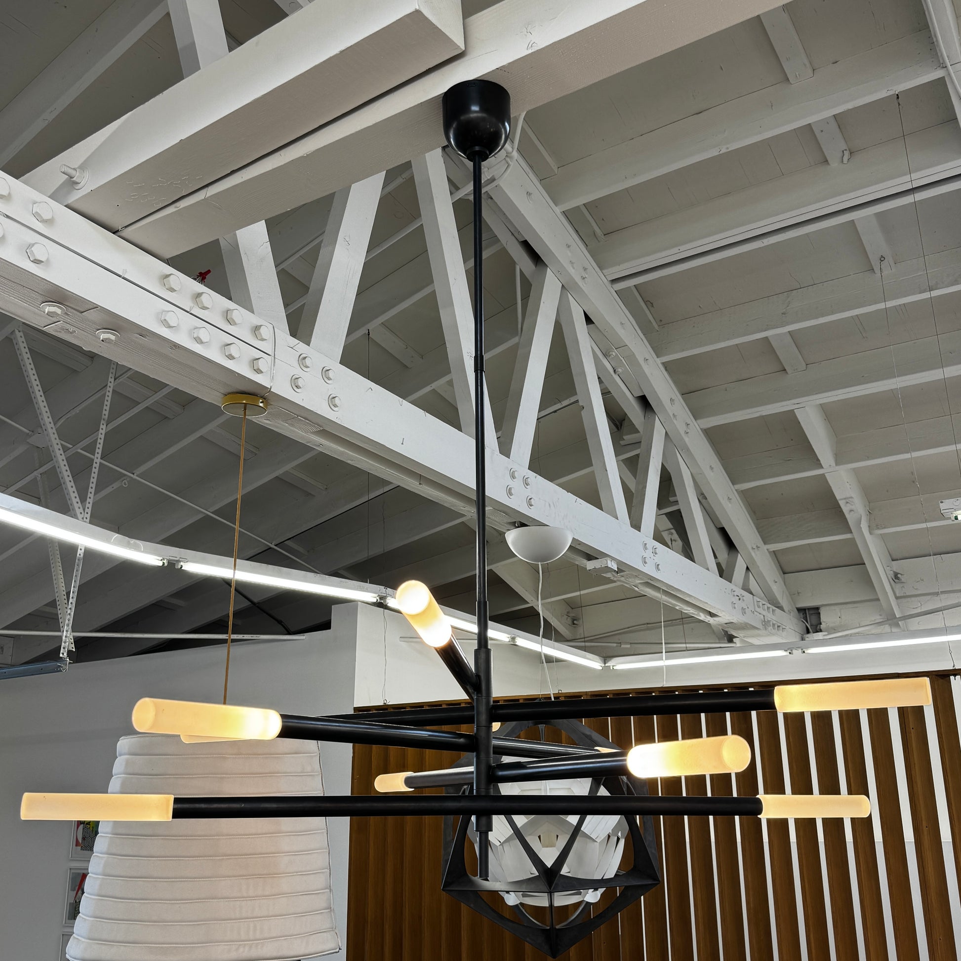 The Visual Comfort Signature Rousseau Grande Ten Light Articulating Chandelier features a modern black design with ten horizontal arms, each ending in a yellow-toned rectangular light, suspended from a central black rod against a white background.