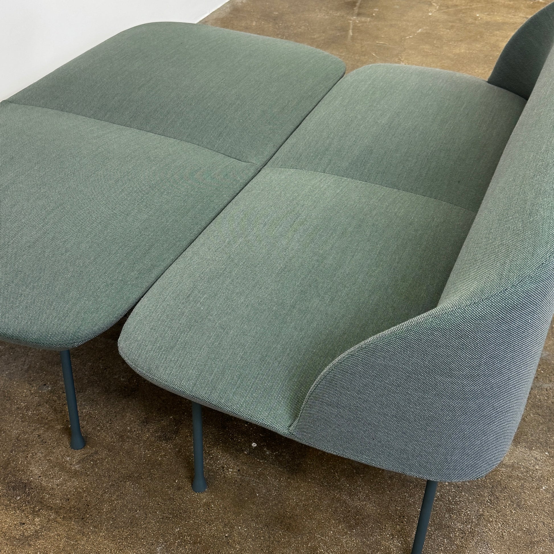 The Muuto Oslo 2-seat sofa & bench by Muuto, featuring modern green upholstery and slim black legs inspired by Danish design, stands in a bright room with beige walls and sheer white curtains.