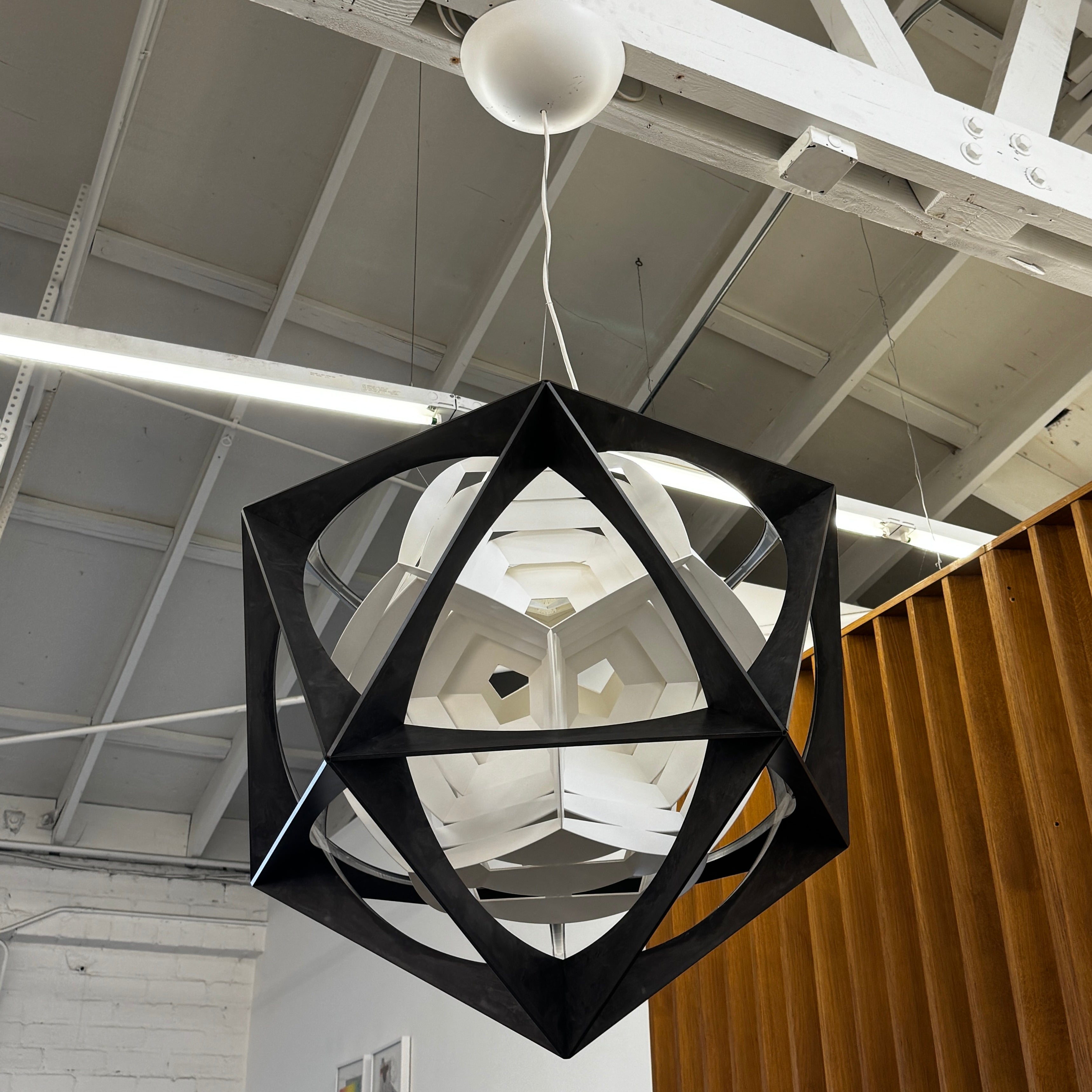 The Louis Poulsen OE Quasi Pendant is a sculptural geometric light fixture featuring a black outer frame and layered white panels, elegantly suspended by a cord—a modern design by Louis Poulsen.