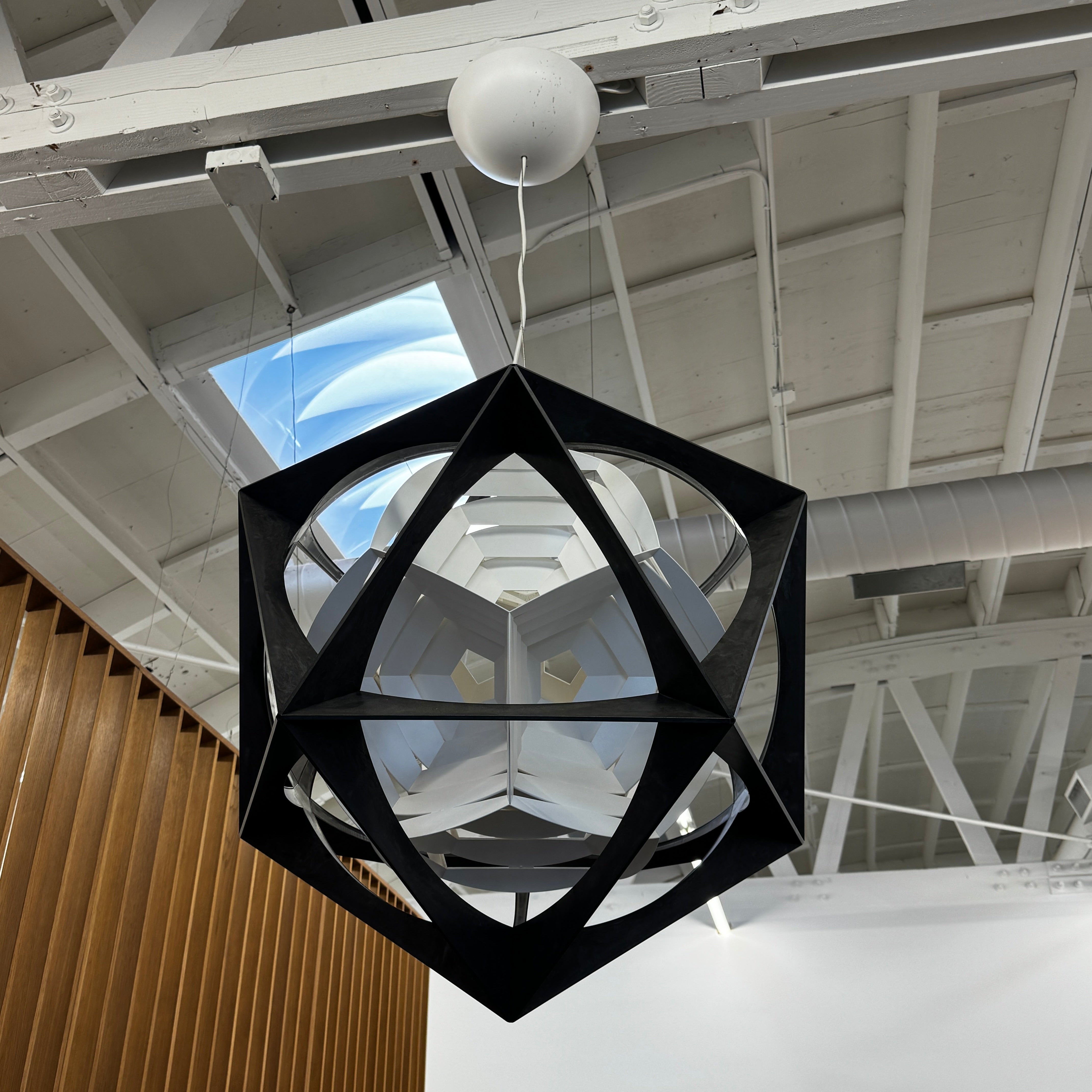 The Louis Poulsen OE Quasi Pendant is a sculptural geometric light fixture featuring a black outer frame and layered white panels, elegantly suspended by a cord—a modern design by Louis Poulsen.