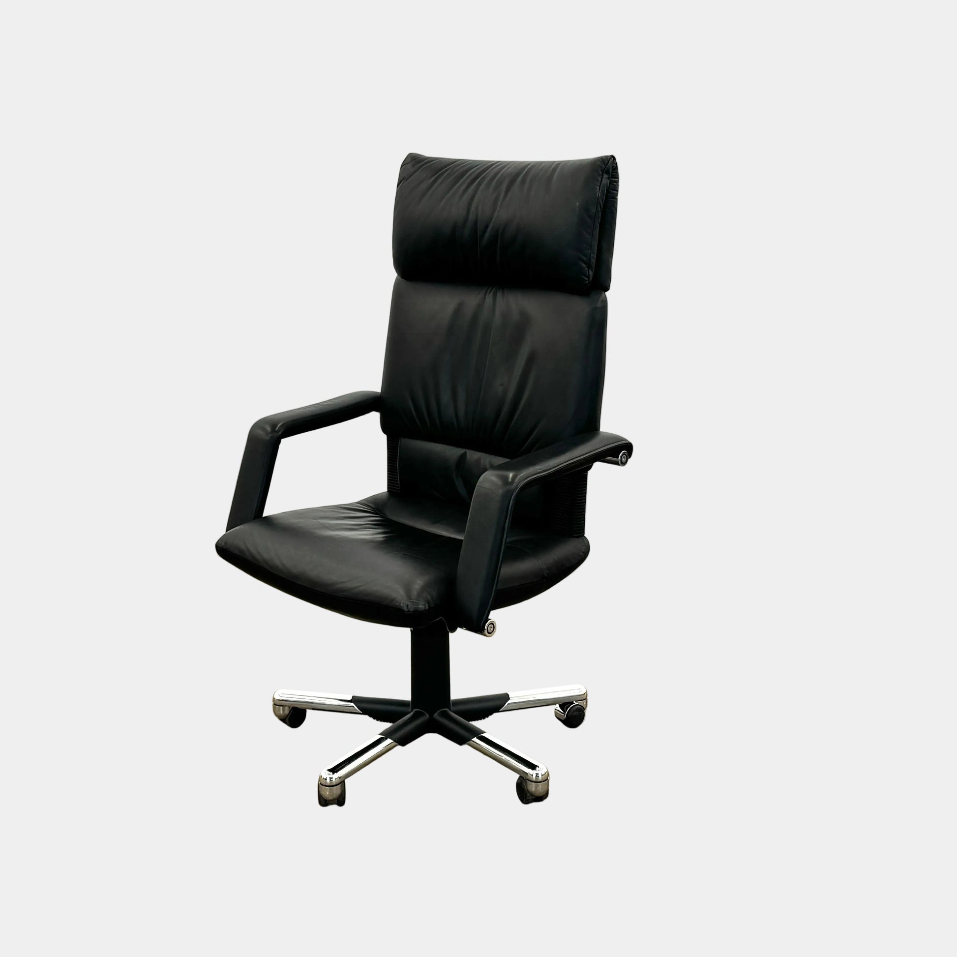 The Vitra Imago office chair by Vitra features black leather, armrests, a high backrest, and a metal five-wheel base, shown here on a concrete floor with a white background.