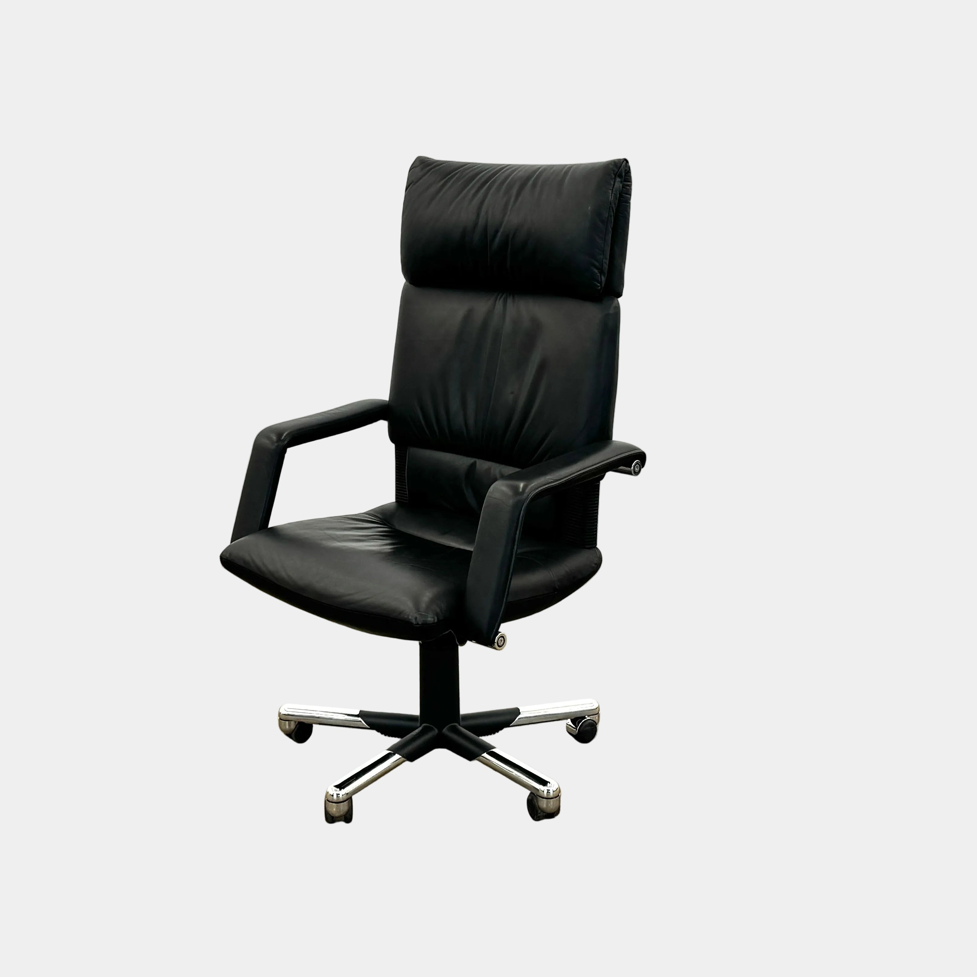 The Vitra Imago office chair by Vitra features black leather, armrests, a high backrest, and a metal five-wheel base, shown here on a concrete floor with a white background.