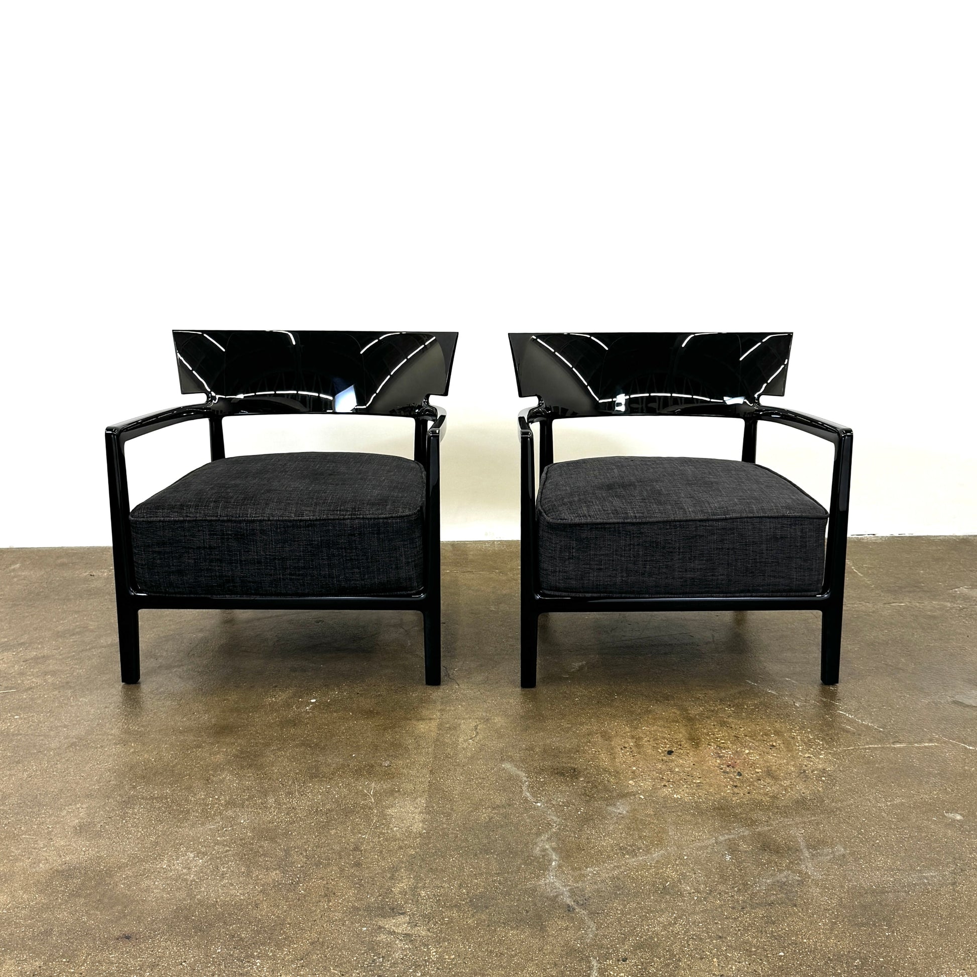 A Kartell Cara Lounge Chair by Kartell, featuring a wide black backrest and dark cushion, rests on a concrete floor in front of a plain white wall.