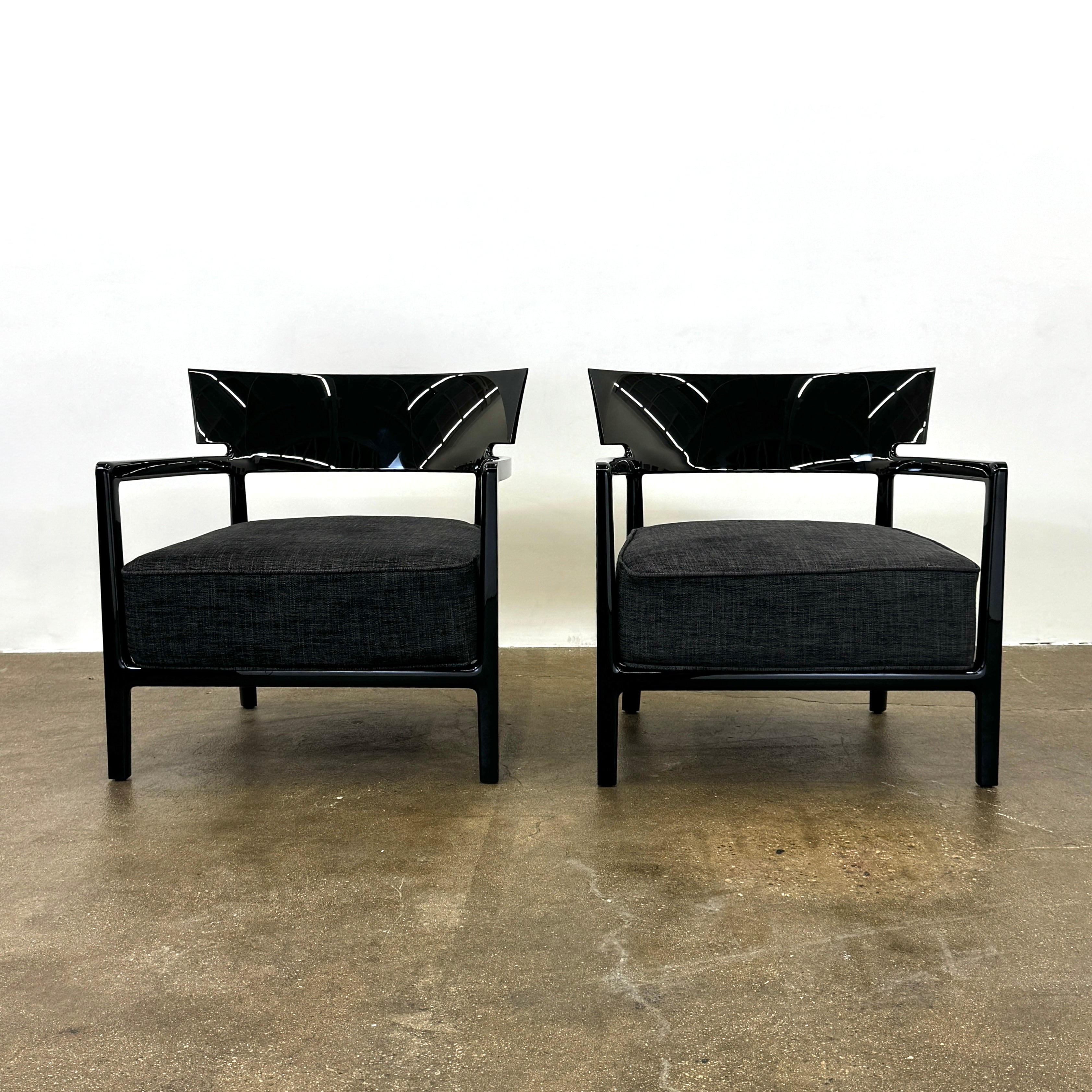 A Kartell Cara Lounge Chair by Kartell, featuring a wide black backrest and dark cushion, rests on a concrete floor in front of a plain white wall.