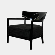 A Kartell Cara Lounge Chair by Kartell, featuring a wide black backrest and dark cushion, rests on a concrete floor in front of a plain white wall.