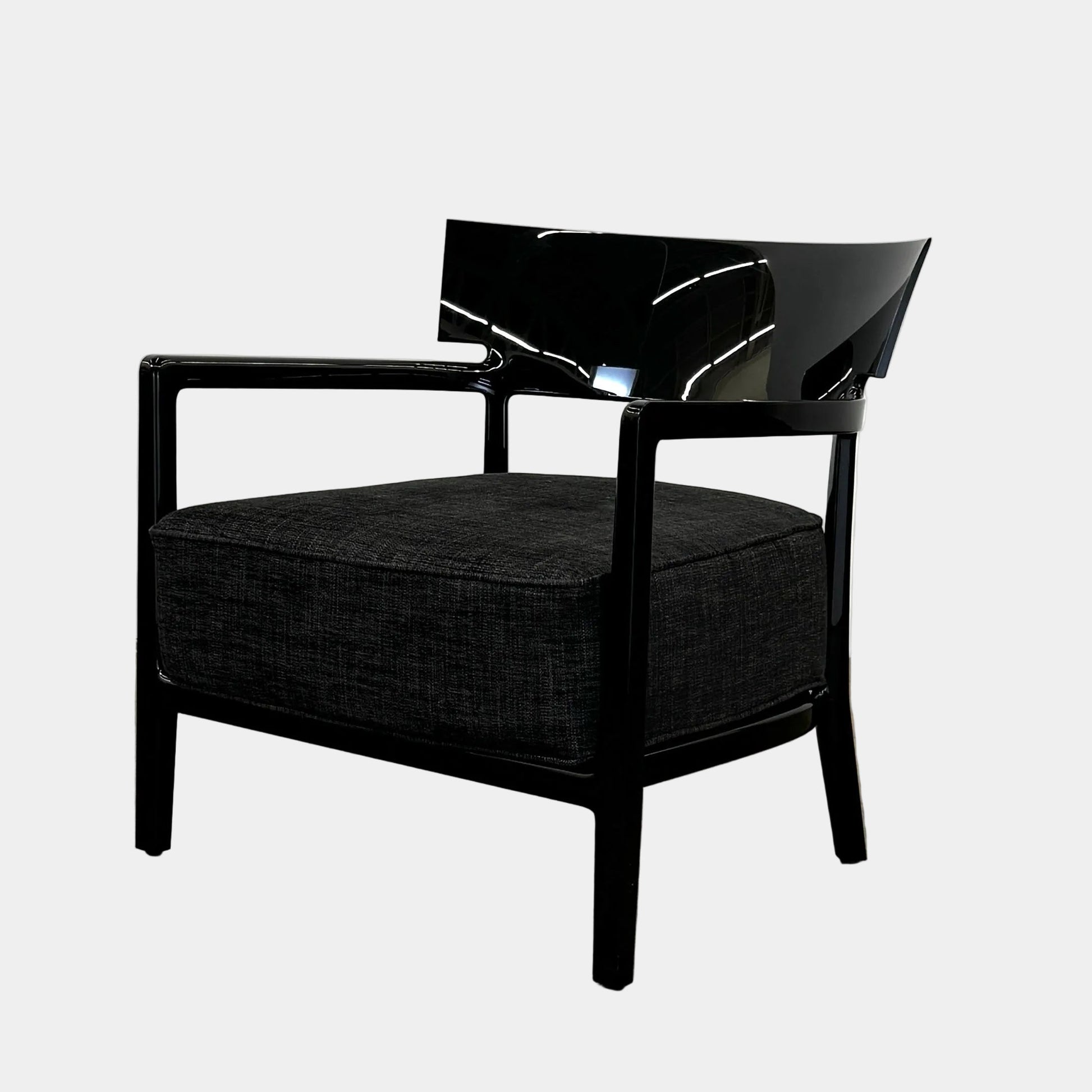 A Kartell Cara Lounge Chair by Kartell, featuring a wide black backrest and dark cushion, rests on a concrete floor in front of a plain white wall.