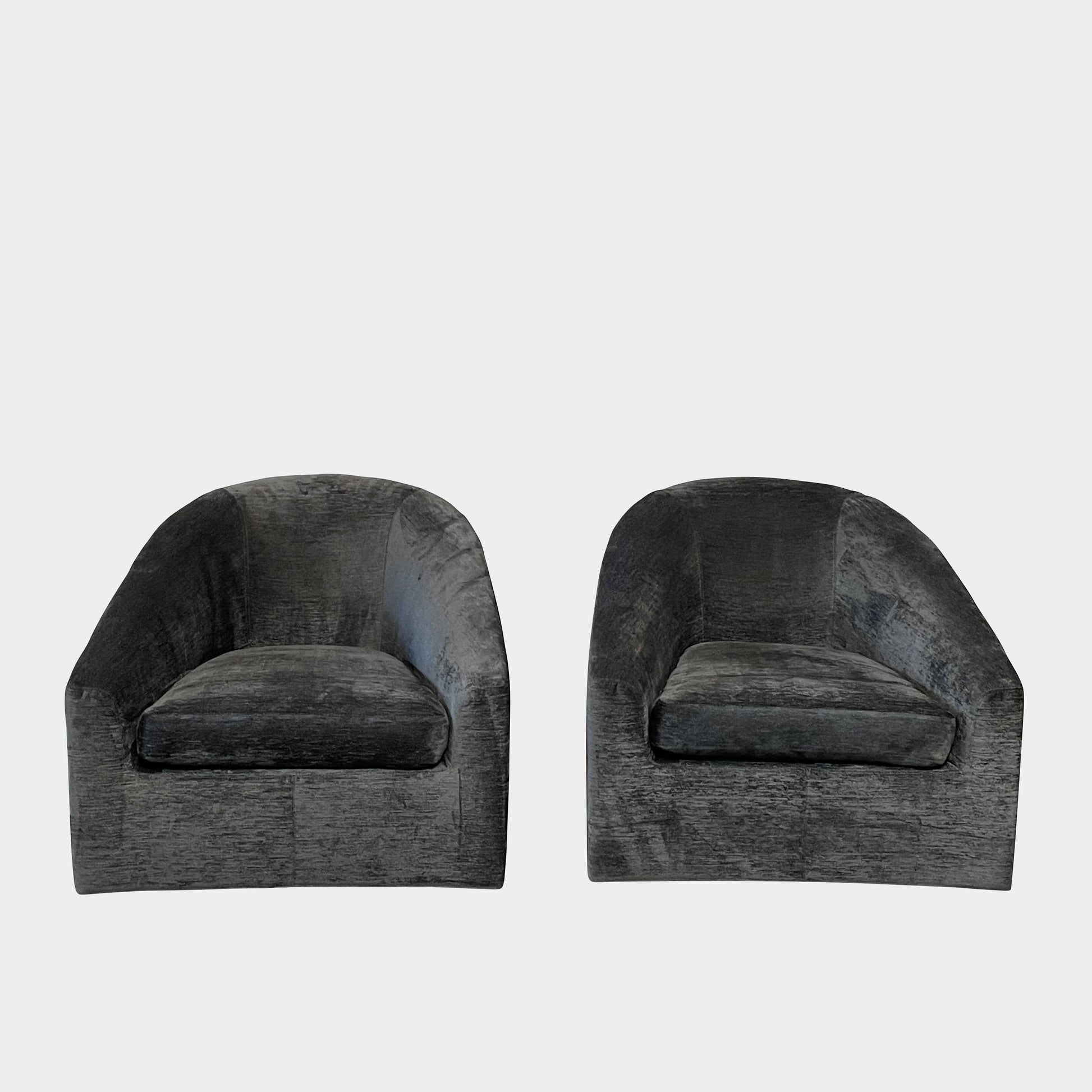 The Minotti Quinn Swivel Lounge Chair Set of 2 showcases a minimalist design with dark gray, curved forms in luxurious chenille. Ideal for the living room, these modern chairs stand out against a light gray backdrop.