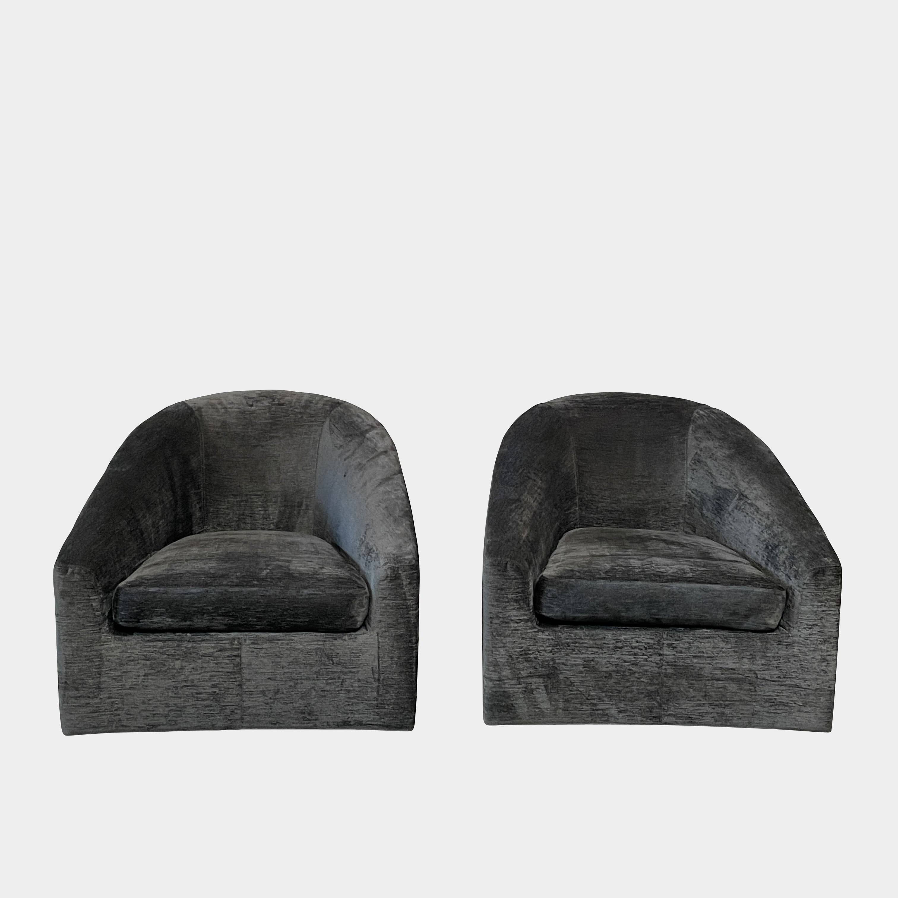 The Minotti Quinn Swivel Lounge Chair Set of 2 showcases a minimalist design with dark gray, curved forms in luxurious chenille. Ideal for the living room, these modern chairs stand out against a light gray backdrop.