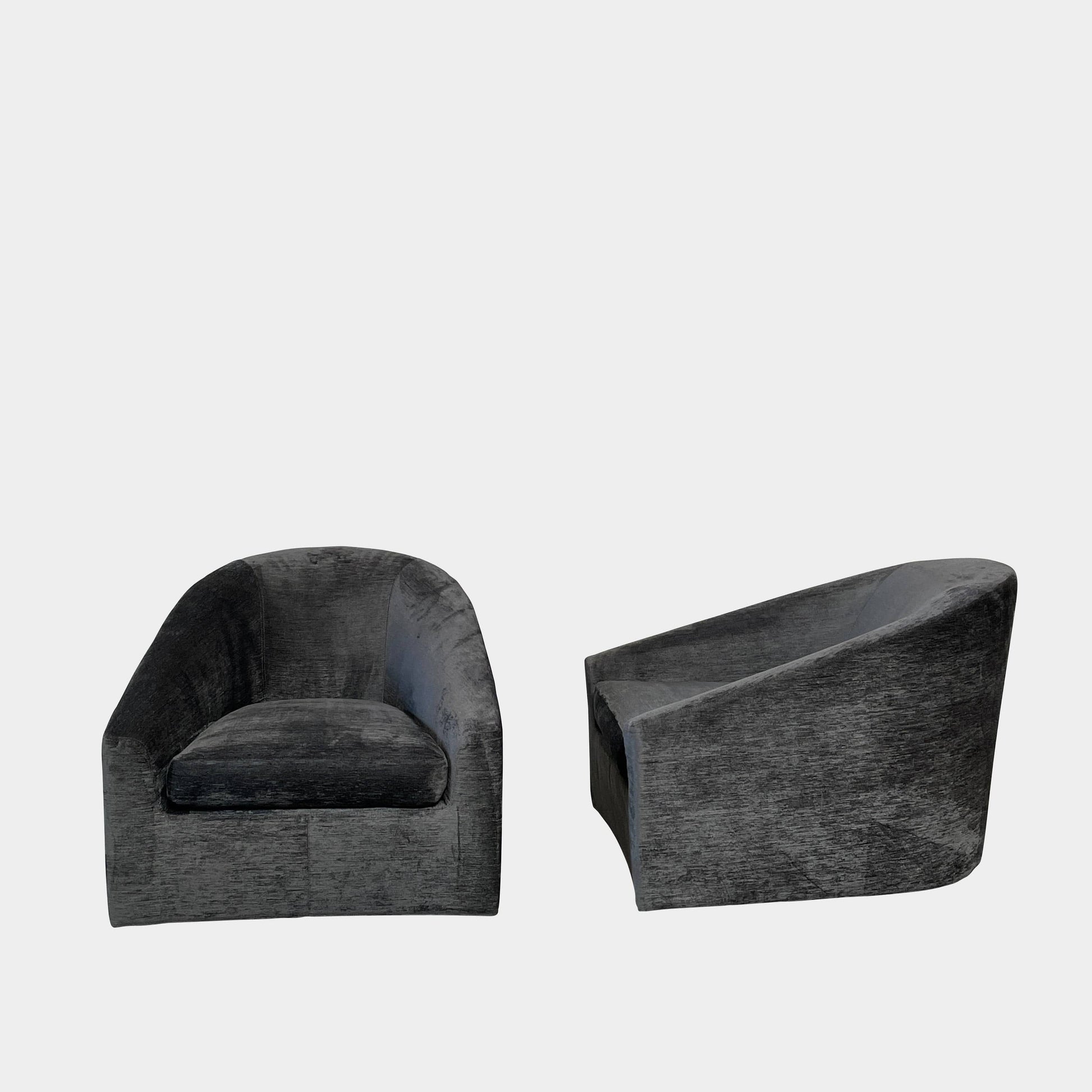 The Minotti Quinn Swivel Lounge Chair Set of 2 showcases a minimalist design with dark gray, curved forms in luxurious chenille. Ideal for the living room, these modern chairs stand out against a light gray backdrop.