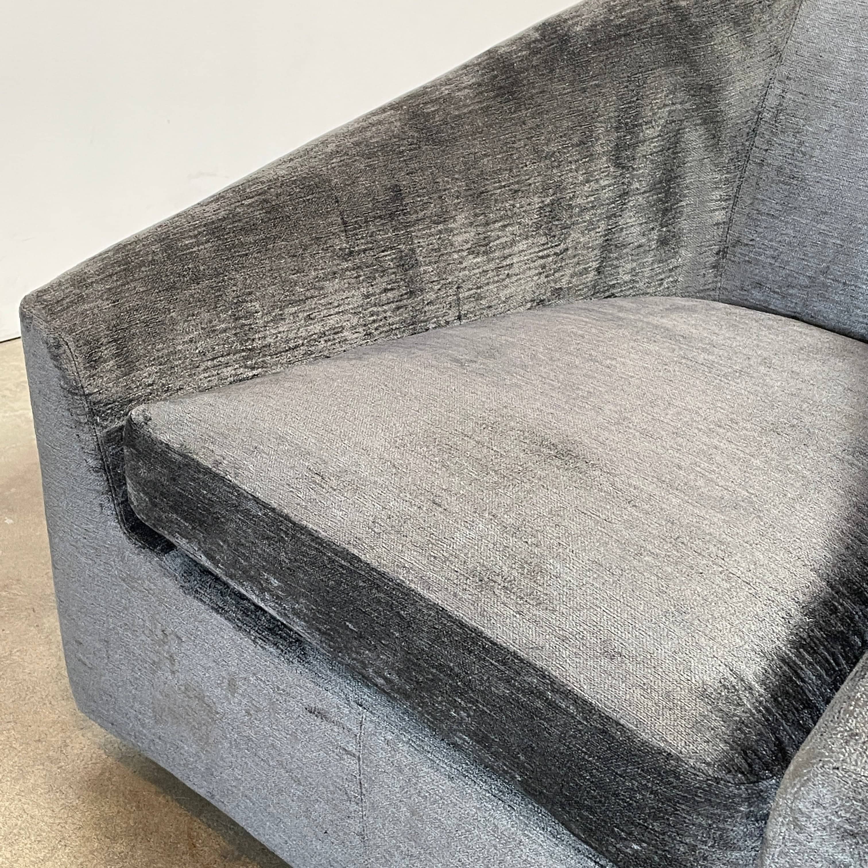 The Minotti Quinn Swivel Lounge Chair Set of 2 showcases a minimalist design with dark gray, curved forms in luxurious chenille. Ideal for the living room, these modern chairs stand out against a light gray backdrop.