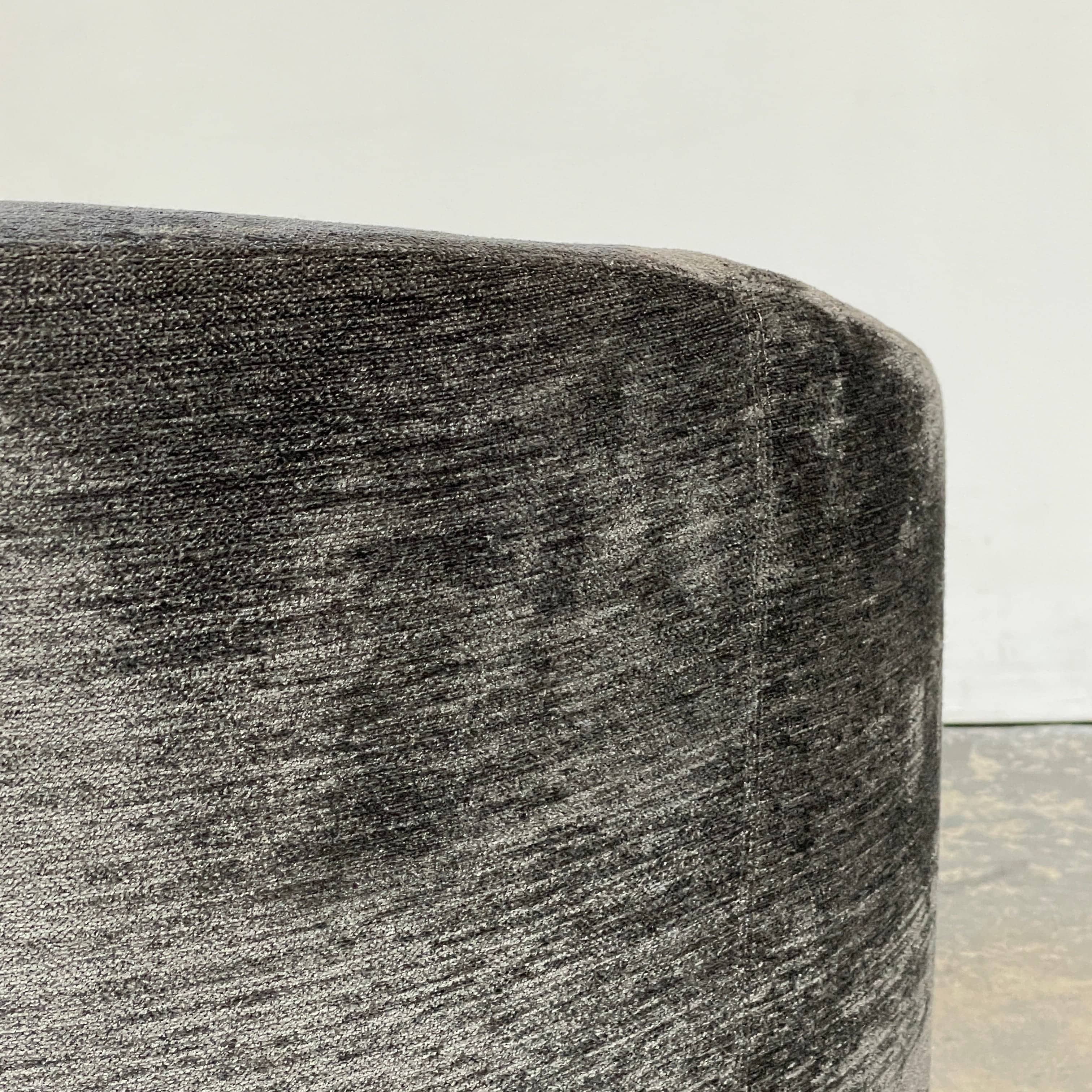 The Minotti Quinn Swivel Lounge Chair Set of 2 showcases a minimalist design with dark gray, curved forms in luxurious chenille. Ideal for the living room, these modern chairs stand out against a light gray backdrop.