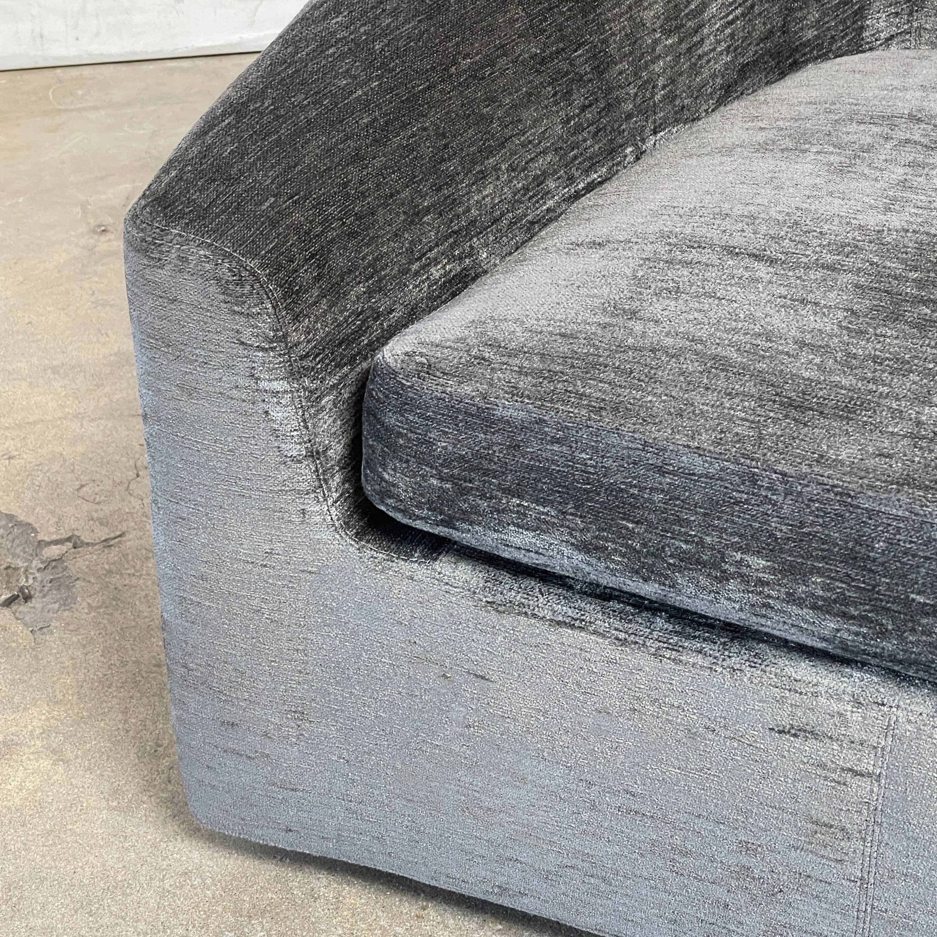 The Minotti Quinn Swivel Lounge Chair Set of 2 showcases a minimalist design with dark gray, curved forms in luxurious chenille. Ideal for the living room, these modern chairs stand out against a light gray backdrop.