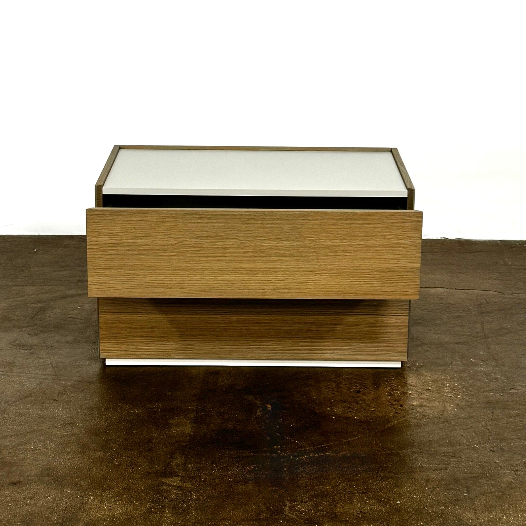 The Sangiacomo Cidori Small Chest of Drawers by Sangiacomo is ideal for contemporary spaces, featuring a light-toned top and single partially open drawer, set on a concrete floor against a white wall.