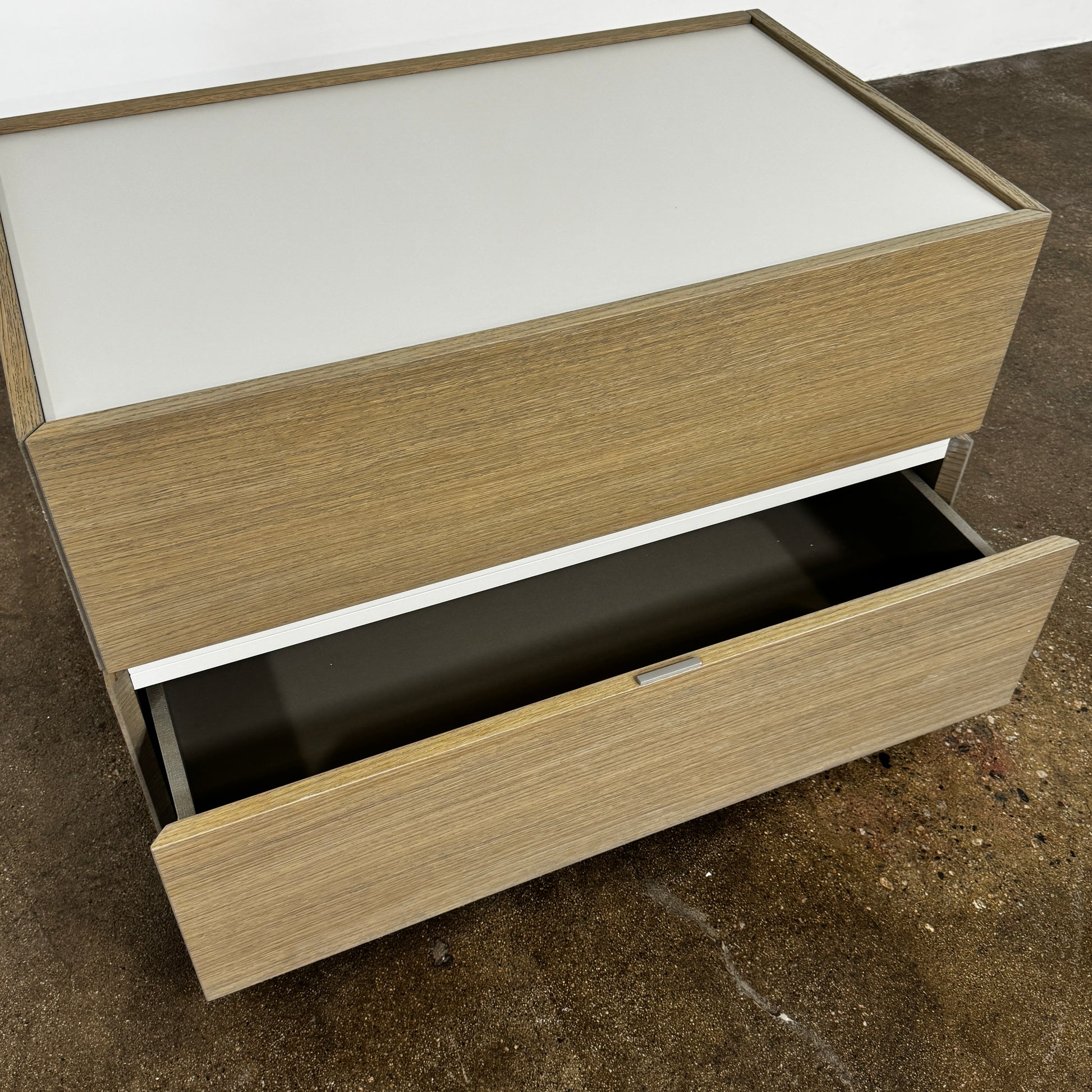 The Sangiacomo Cidori Small Chest of Drawers by Sangiacomo is ideal for contemporary spaces, featuring a light-toned top and single partially open drawer, set on a concrete floor against a white wall.