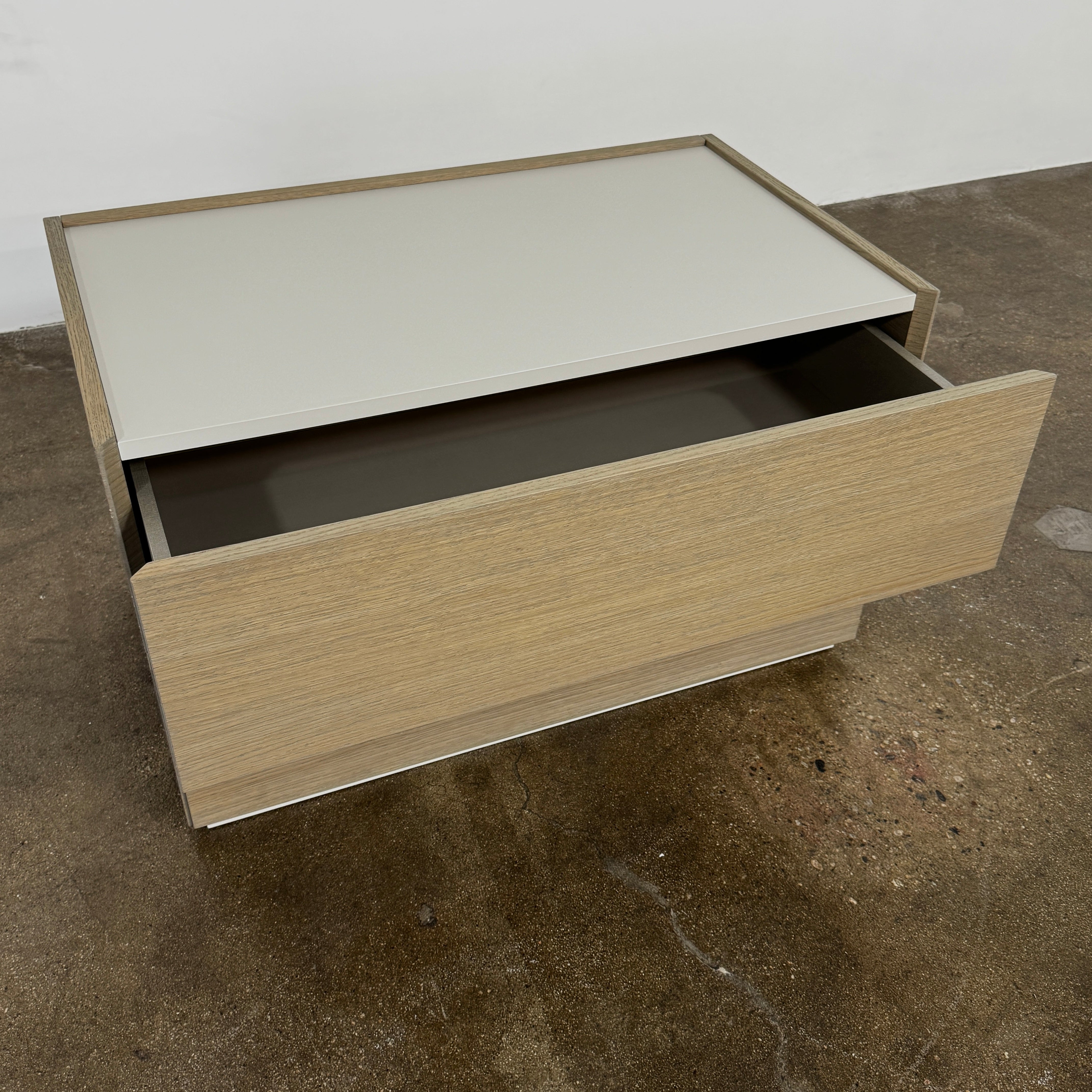 The Sangiacomo Cidori Small Chest of Drawers by Sangiacomo is ideal for contemporary spaces, featuring a light-toned top and single partially open drawer, set on a concrete floor against a white wall.