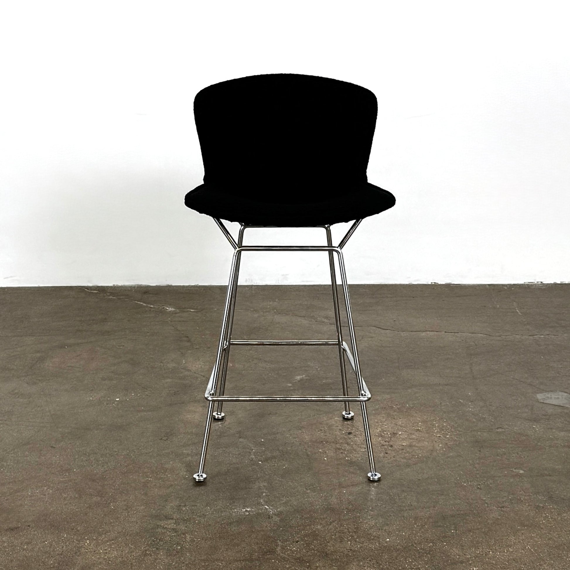 Close-up of a Knoll Bertoia Counter Stool from a set of 4, featuring a black cushion and textured black fabric over the backrest, placed on a polished concrete floor.